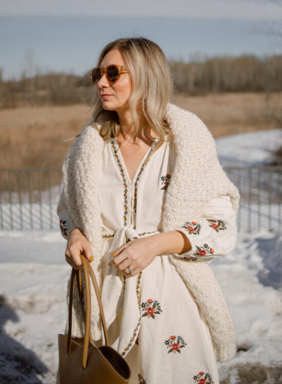 Karin Emily wears a floral spring dress with a chunky knit over her shoulders and a little liffner tulip bag