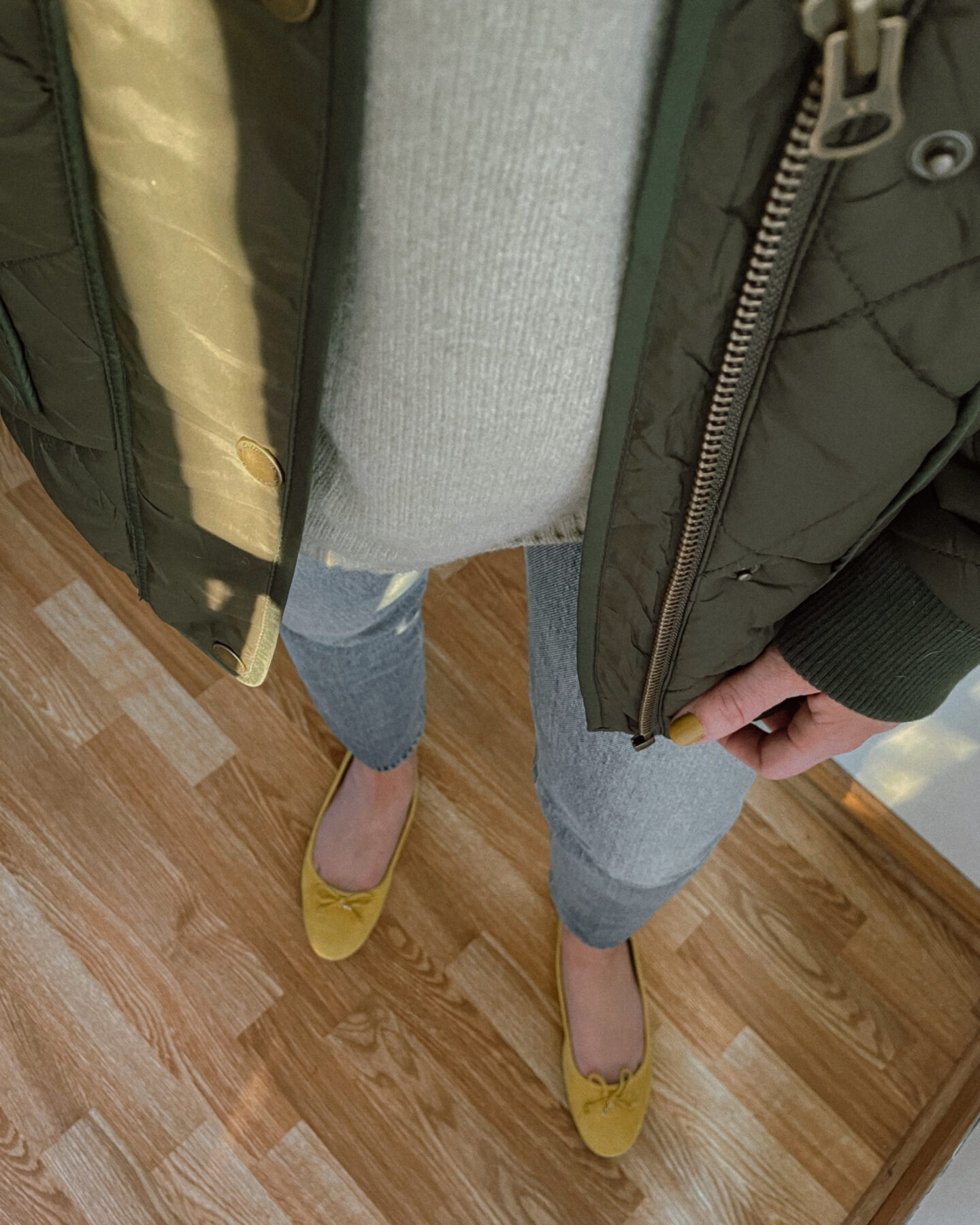 Karin Emily wears a sage green sweater, olive green shirt jacket, light wash straight leg jeans, and yellow ballet flat