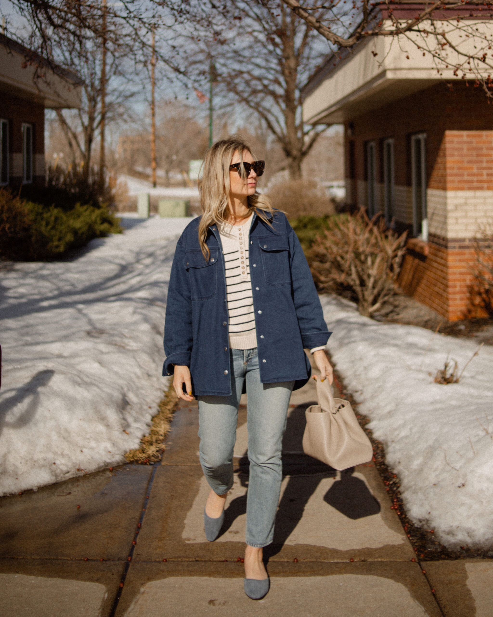 Karin Emily wears a Breton stripe sweater under a denim shirt jacket paired with a pair of light wash jeans and a blue suede pair of mules