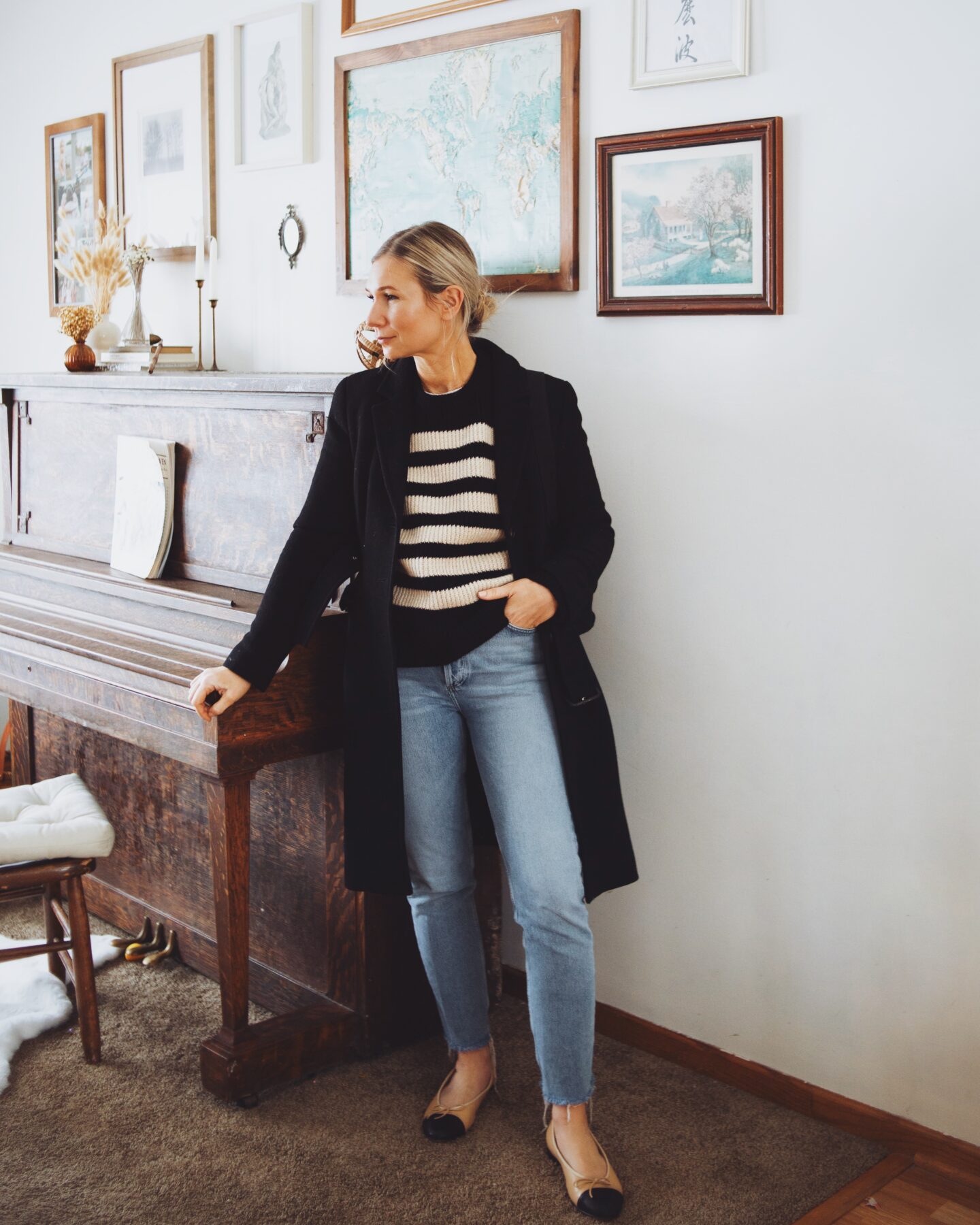 Karin Emily wears a Breton stripe cashmere sweater, Agolde jeans, a black wool belted coat, and Chanel inspired cap toe flats