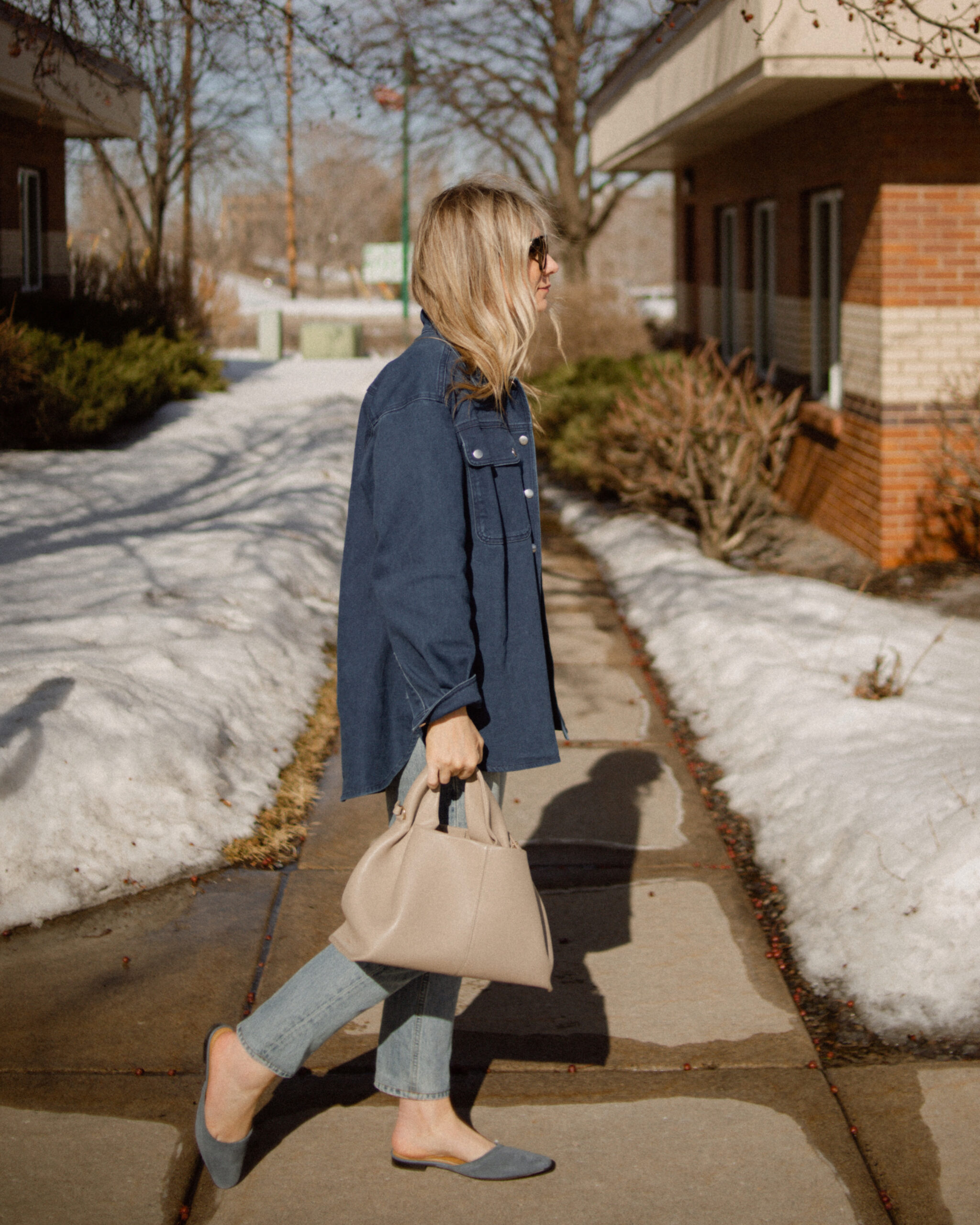 Karin Emily wears a Breton stripe sweater under a denim shirt jacket paired with a pair of light wash jeans and a blue suede pair of mules