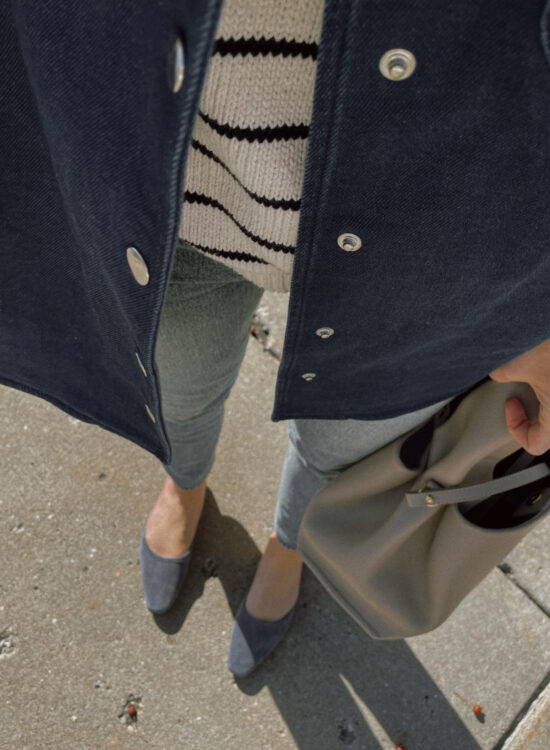 Karin Emily has an update for spring and wears a blue denim shirt jacket, breton stripe sweater, light wash jeans, and blue suede mules