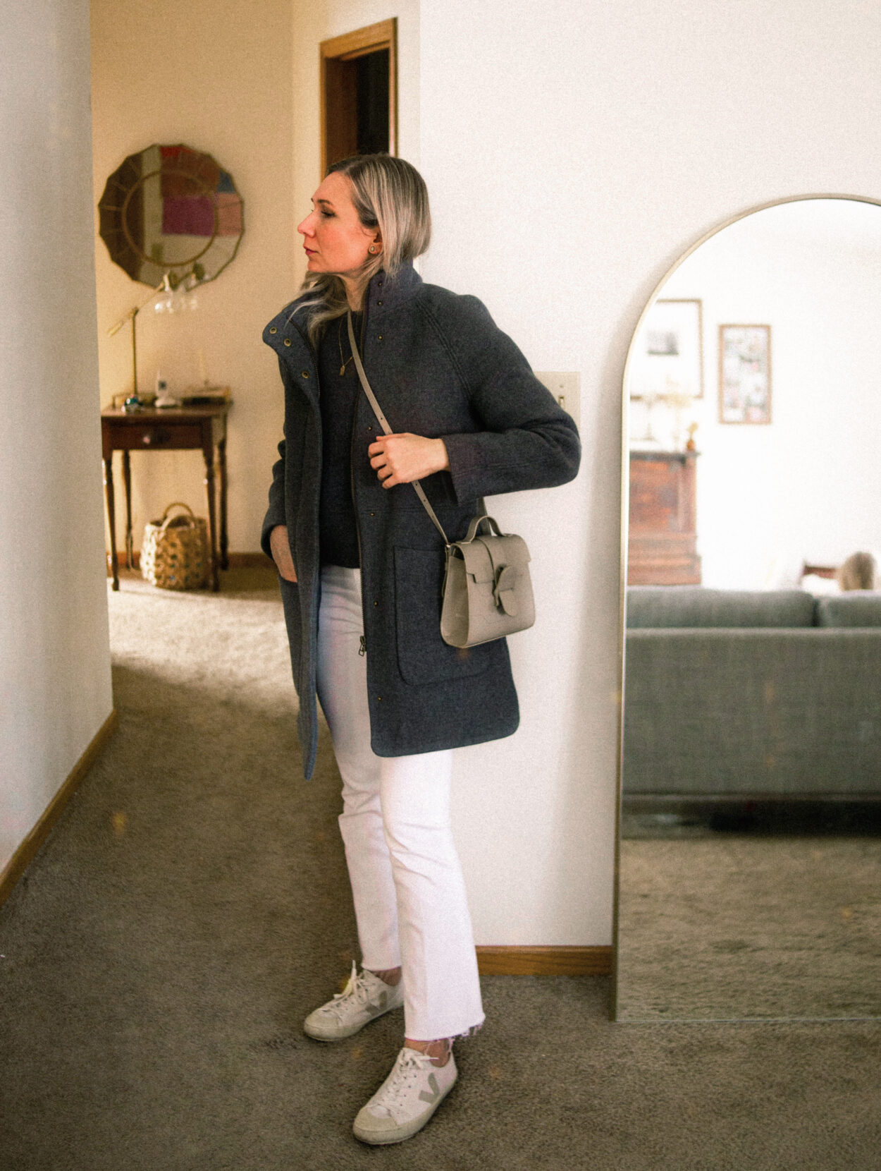 Karin Emily is dressed like the winter sky with a gray wool coat, gray wool sweater, white jeans, and veja canvas sneakers