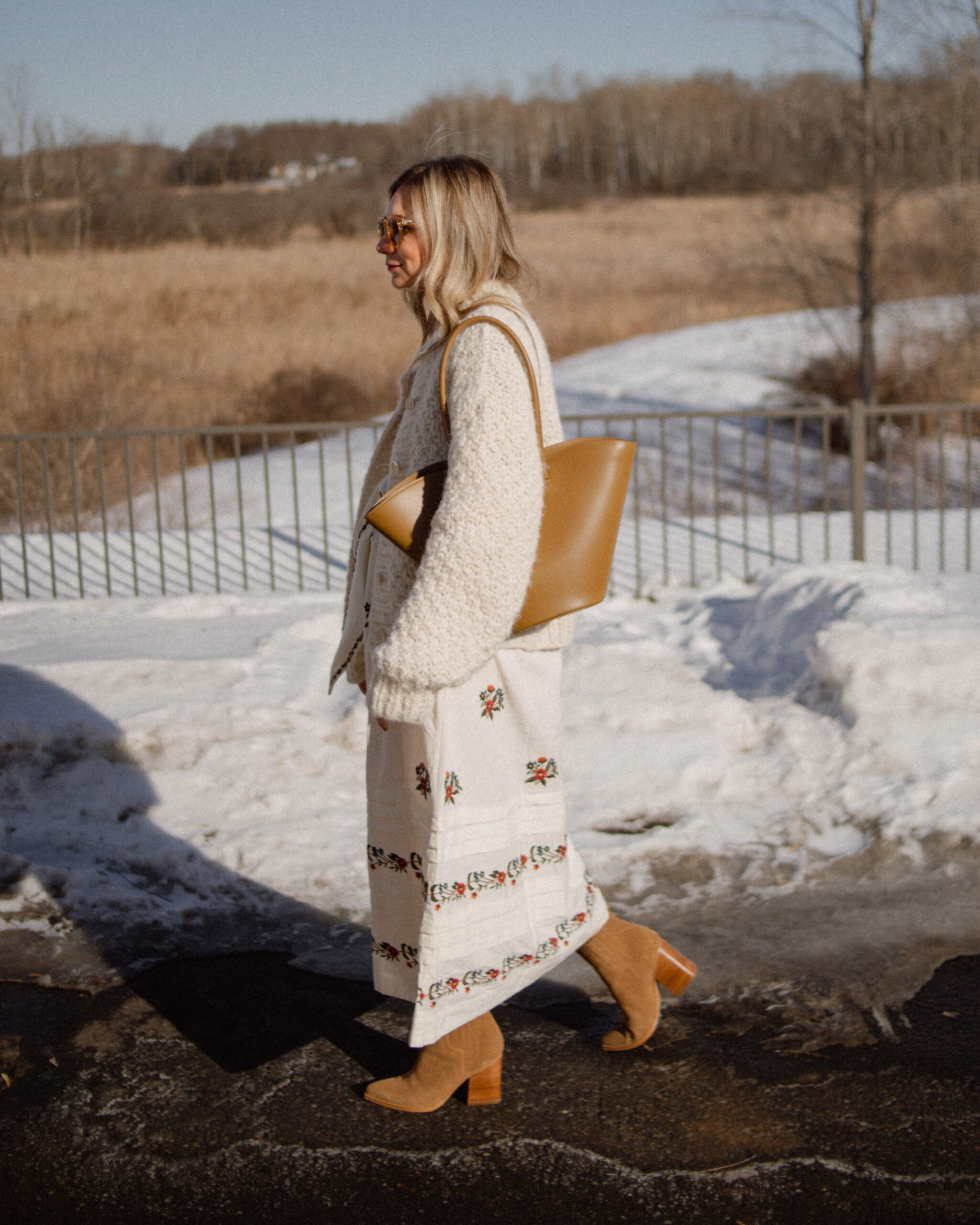 Karin Emily wears a floral spring dress with a chunky knit over her shoulders and a little liffner tulip bag