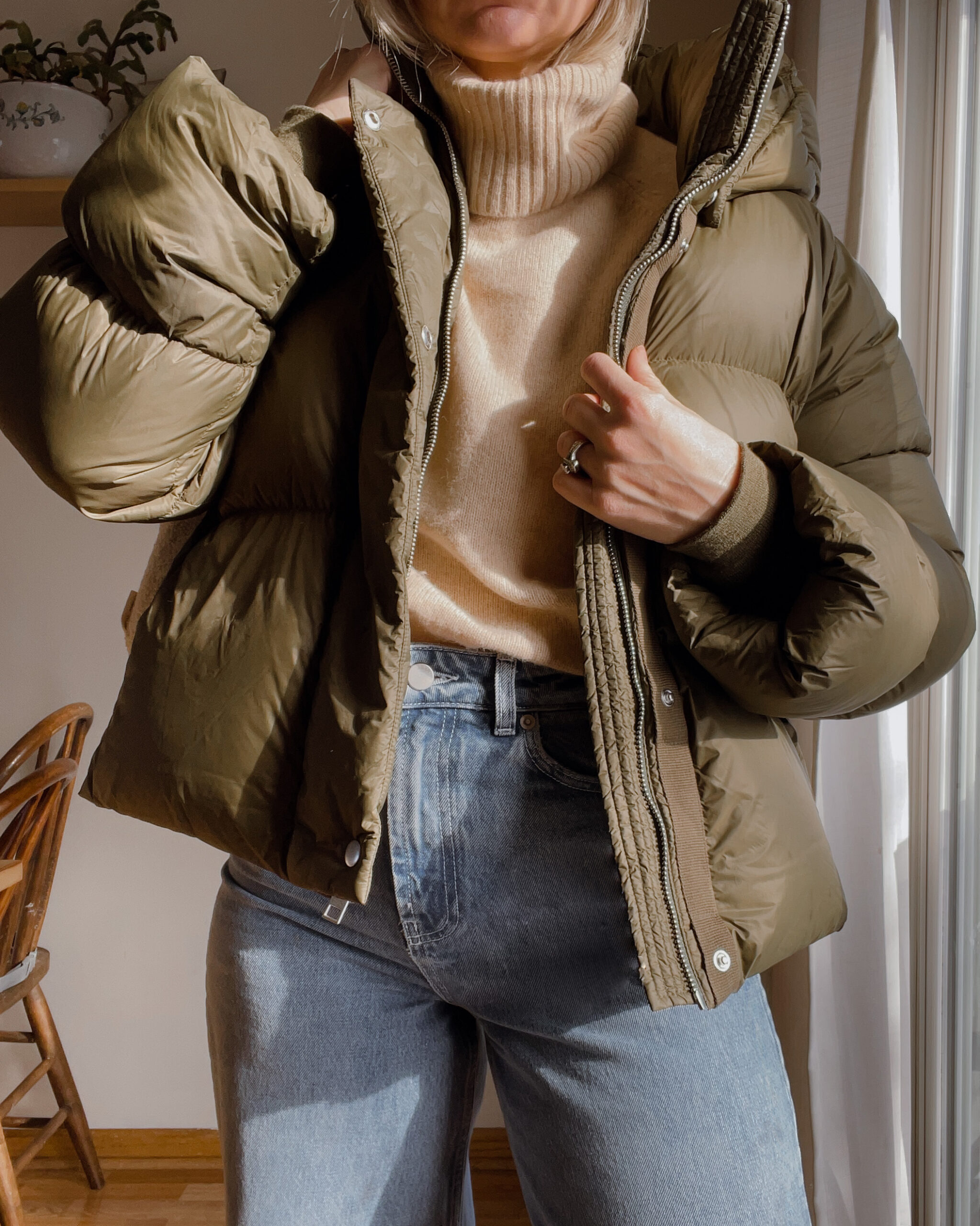 Karin Emily wears a cropped army green puffer coat, cream turtleneck sweater and wide leg jeans,
