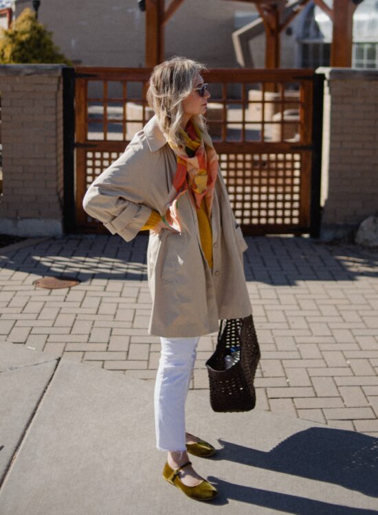 Karin Emily wears a A Classic Trench Coat with a Twist , white jeans, yellow sweater, colorful silk scarf, and green mary jane flats