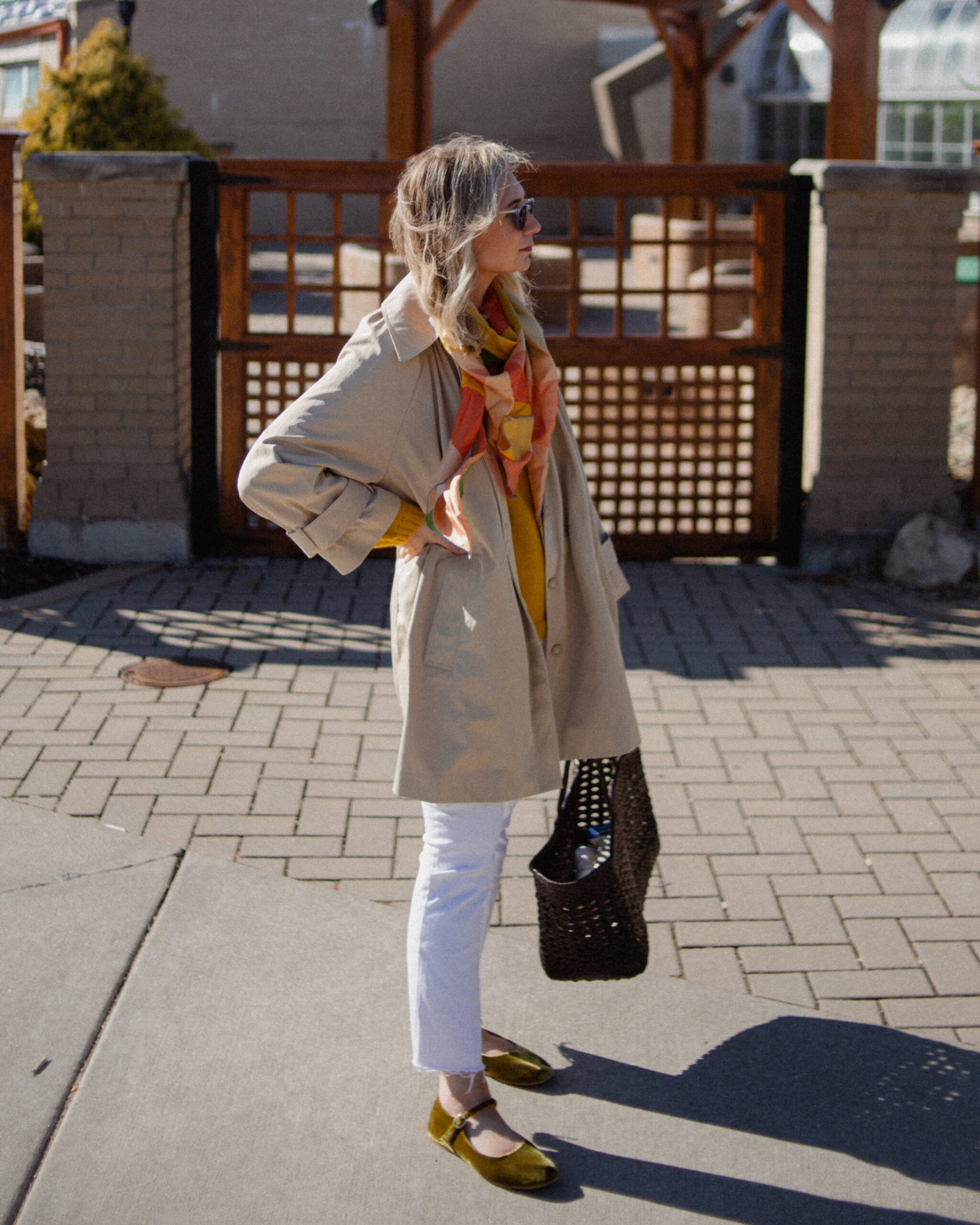 Karin Emily wears a A Classic Trench Coat with a Twist , white jeans, yellow sweater, colorful silk scarf, and green mary jane flats