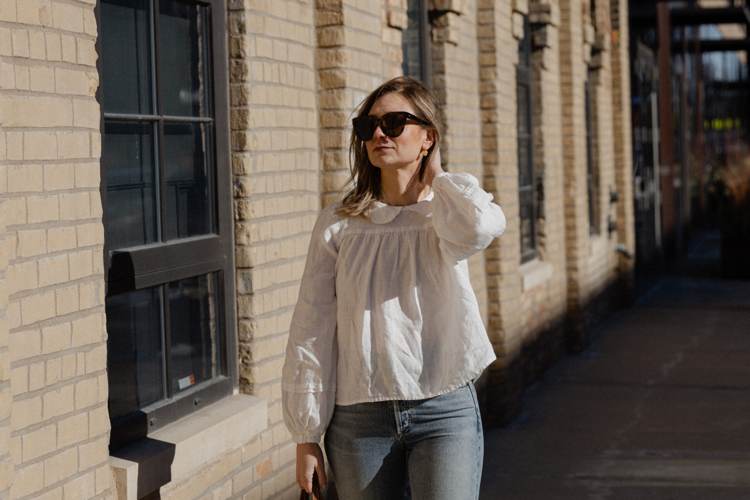 Karin Emily wears a white linen peter pan collar shirt with a pair of light wash straight leg jeans, , and an oversized polene tote bag