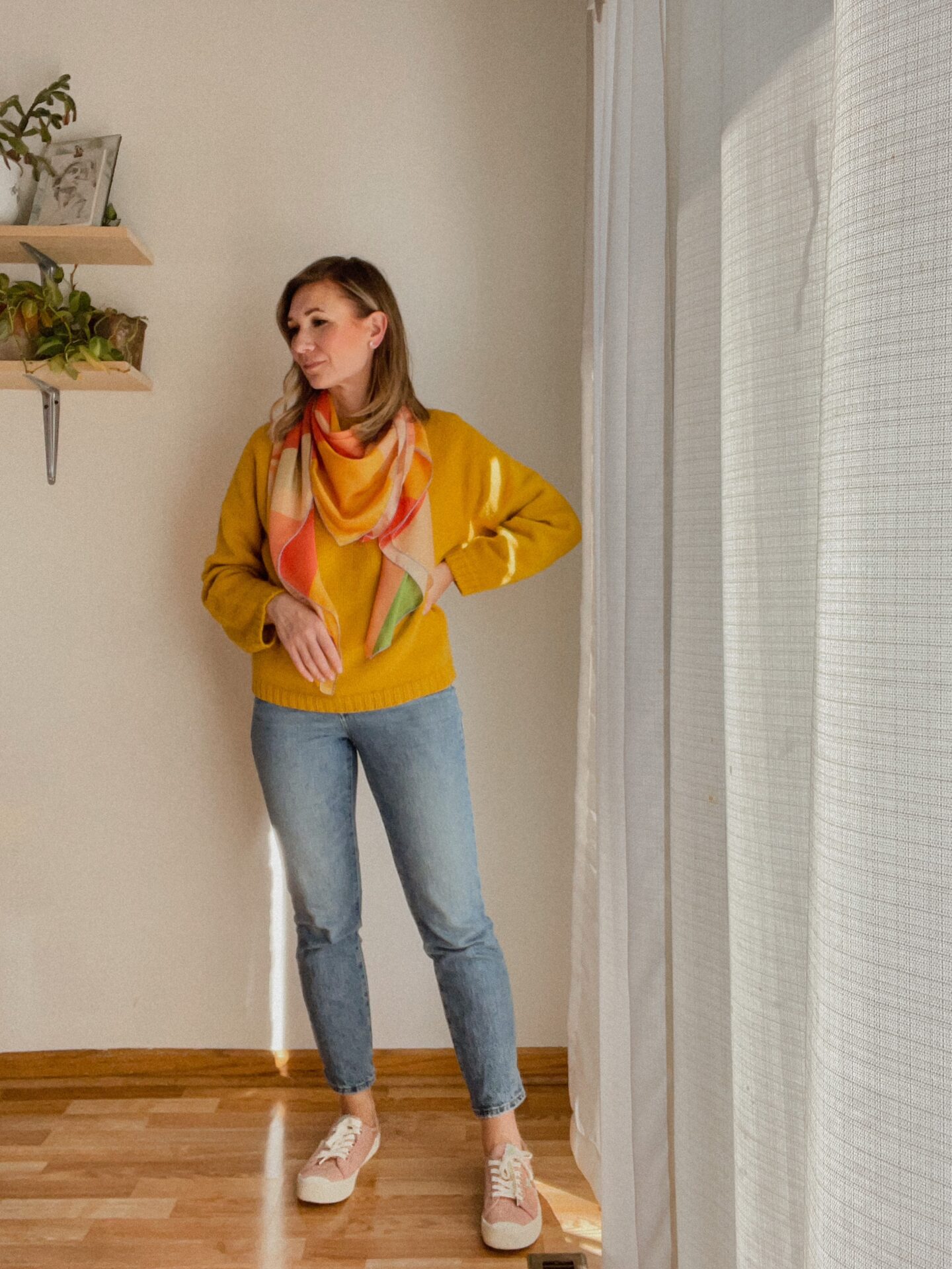 Karin Emily wears a yellow sweater with a bright silk scarf over it, madewell perfect vintage jeans, and pink canvas sneakers