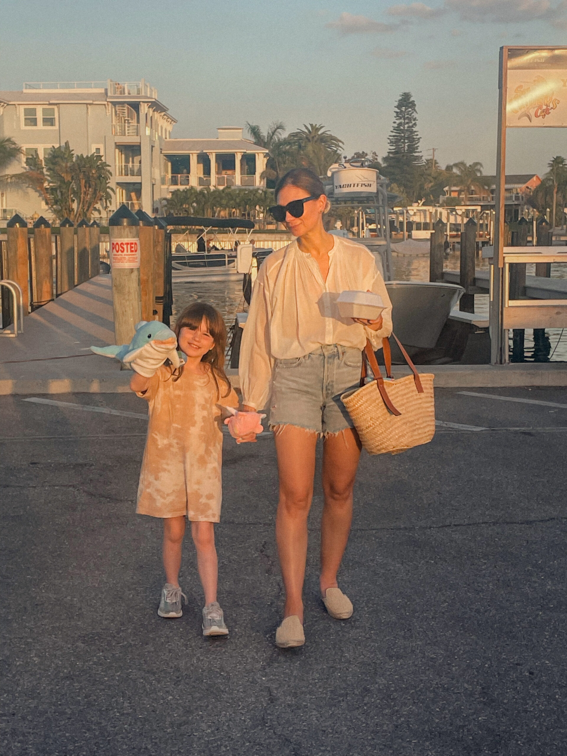 Karin Emily wears resort wear:  a pair of cut off denim shorts, a doen jane blouse, espadrille mules, and a basket bag with her daughter who's wearing a tie dye dress