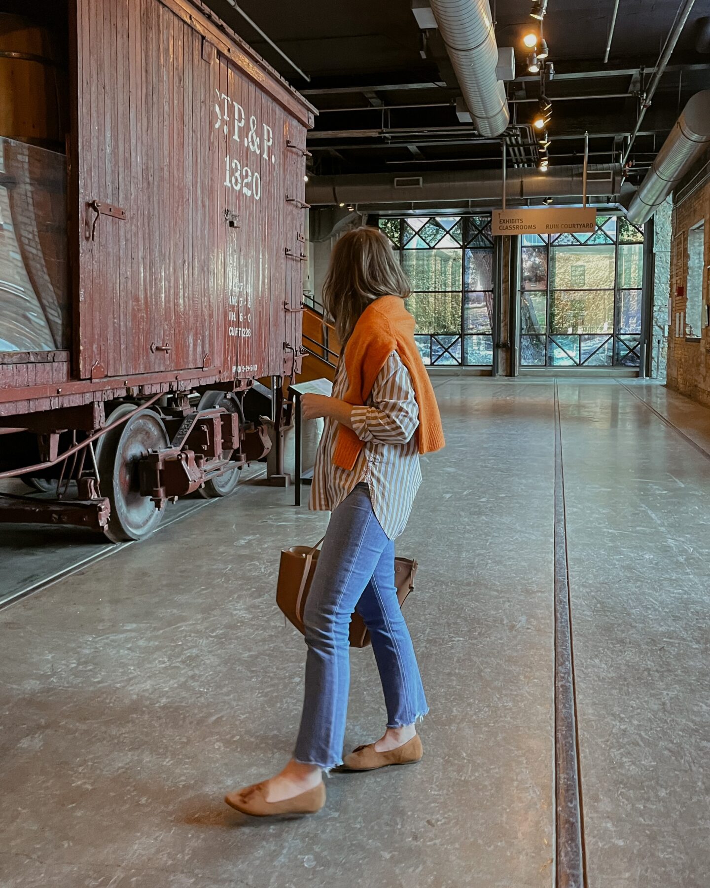 Karin Emily wears a brightly colored striped button down and orange sweater with a comfy pair of jeans and loafers