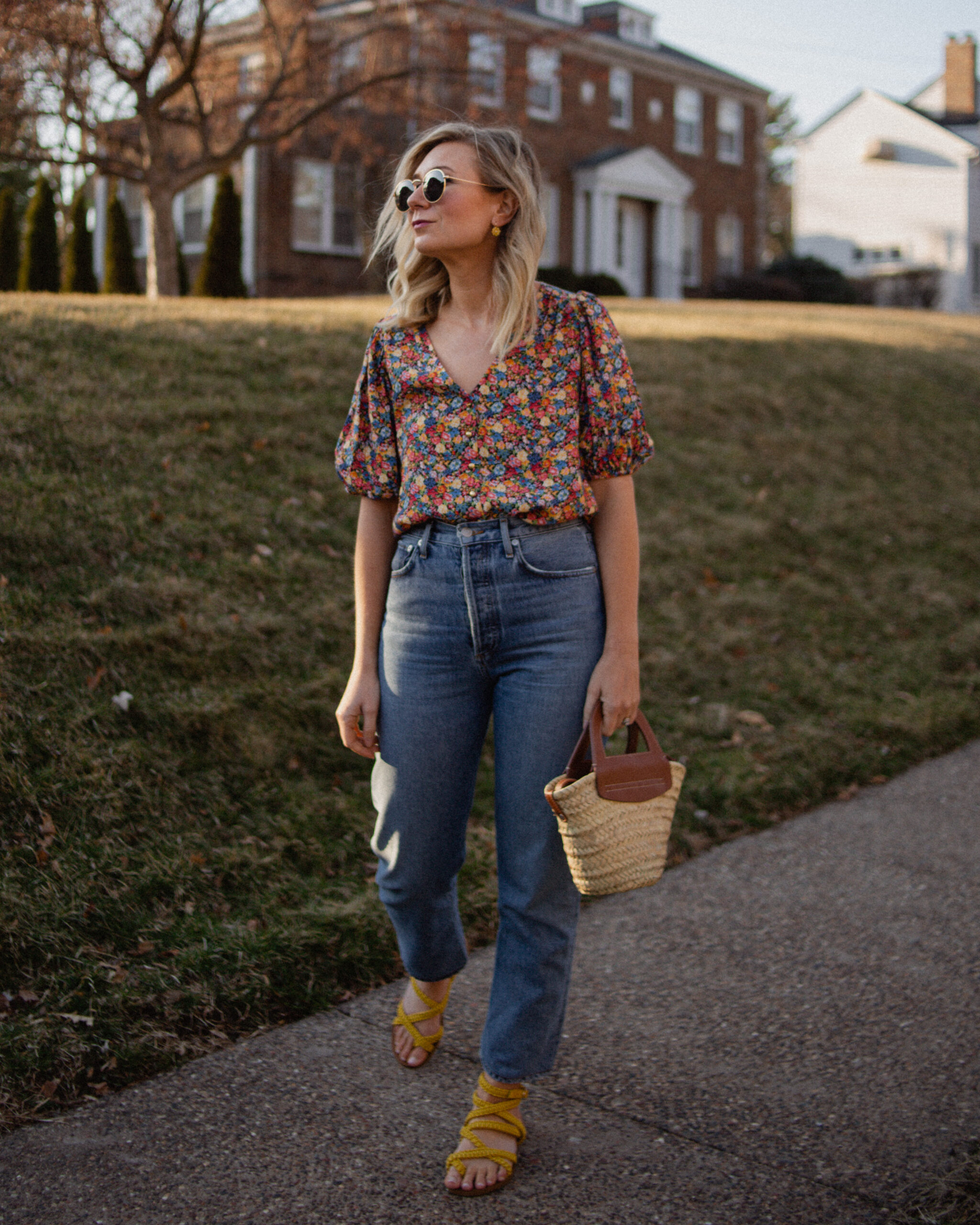 Karin Emily wears a floral top and yellow sandals from Sezane paired with a straight leg pair of jeans from Agolde
