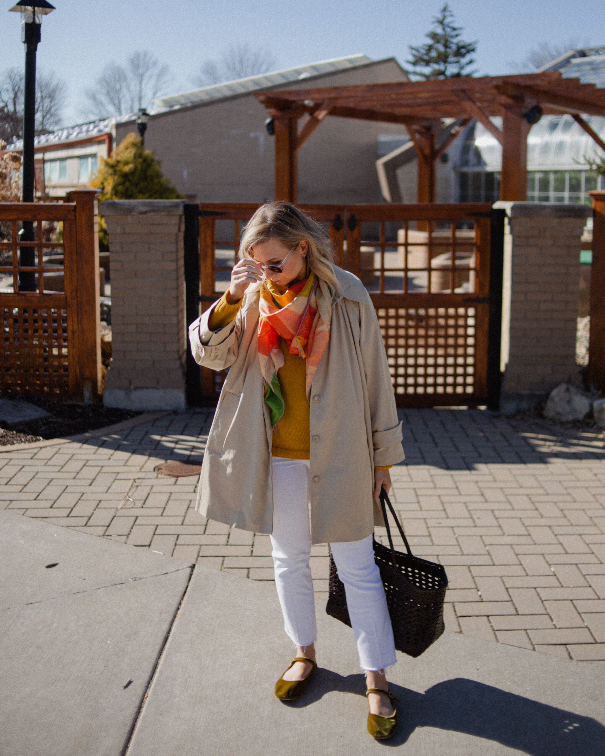 Karin Emily wears a A Classic Trench Coat with a Twist , white jeans, yellow sweater, colorful silk scarf, and green mary jane flats