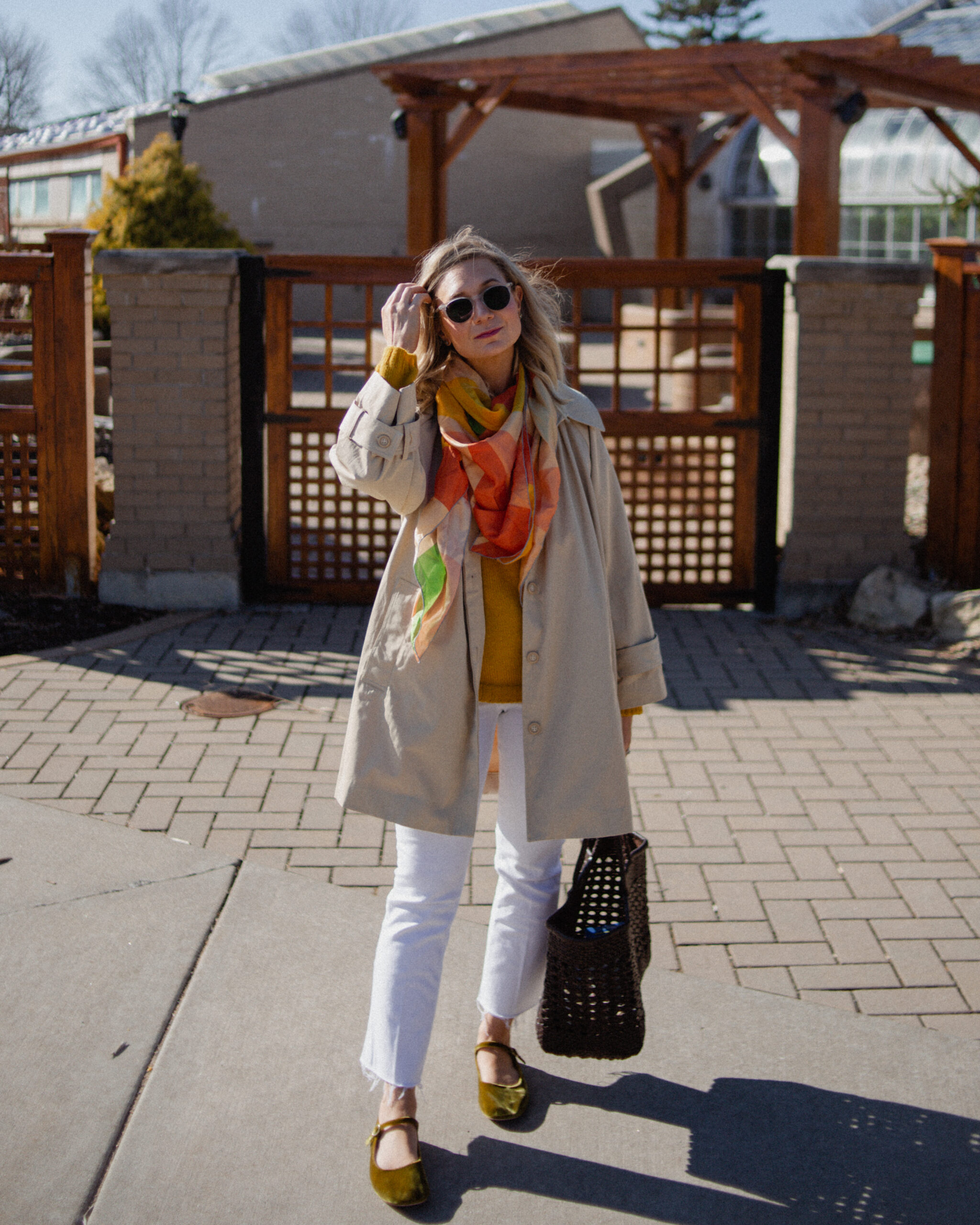 Karin Emily wears a A Classic Trench Coat with a Twist , white jeans, yellow sweater, colorful silk scarf, and green mary jane flats