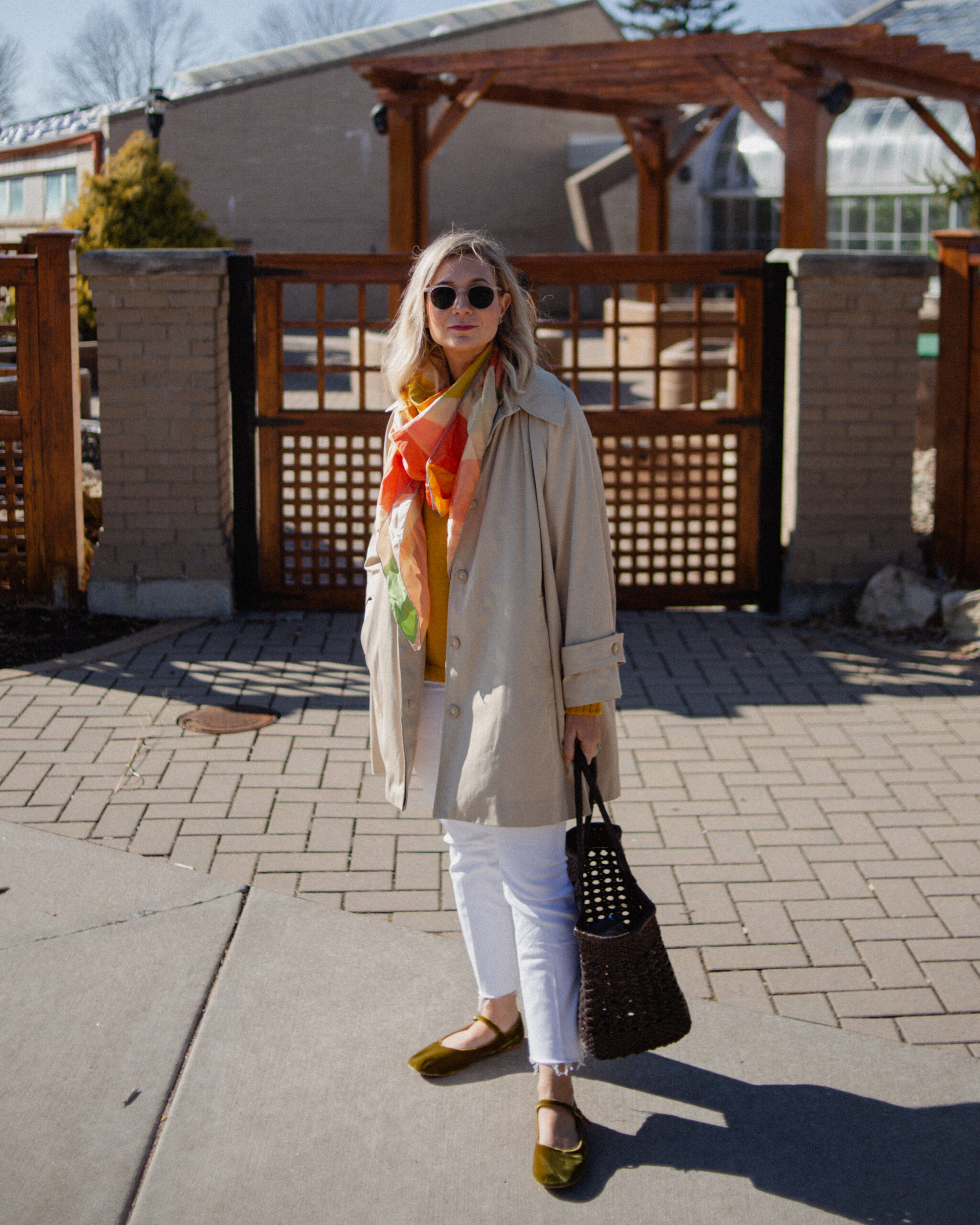 Karin Emily wears a A Classic Trench Coat with a Twist , white jeans, yellow sweater, colorful silk scarf, and green mary jane flats