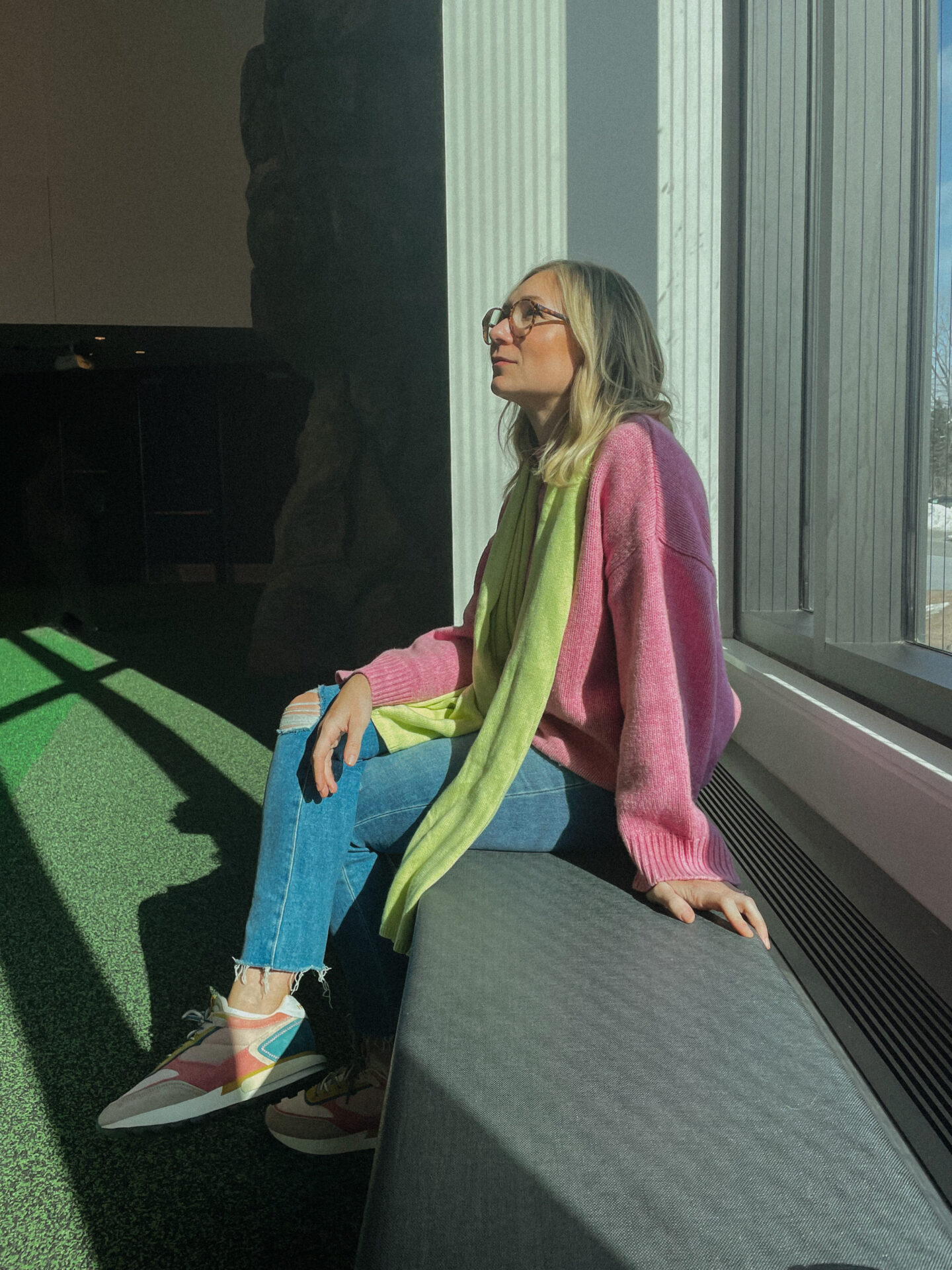 Karin Emily wears bright colors: green scarf, pink sweater, and rainbow sneakers