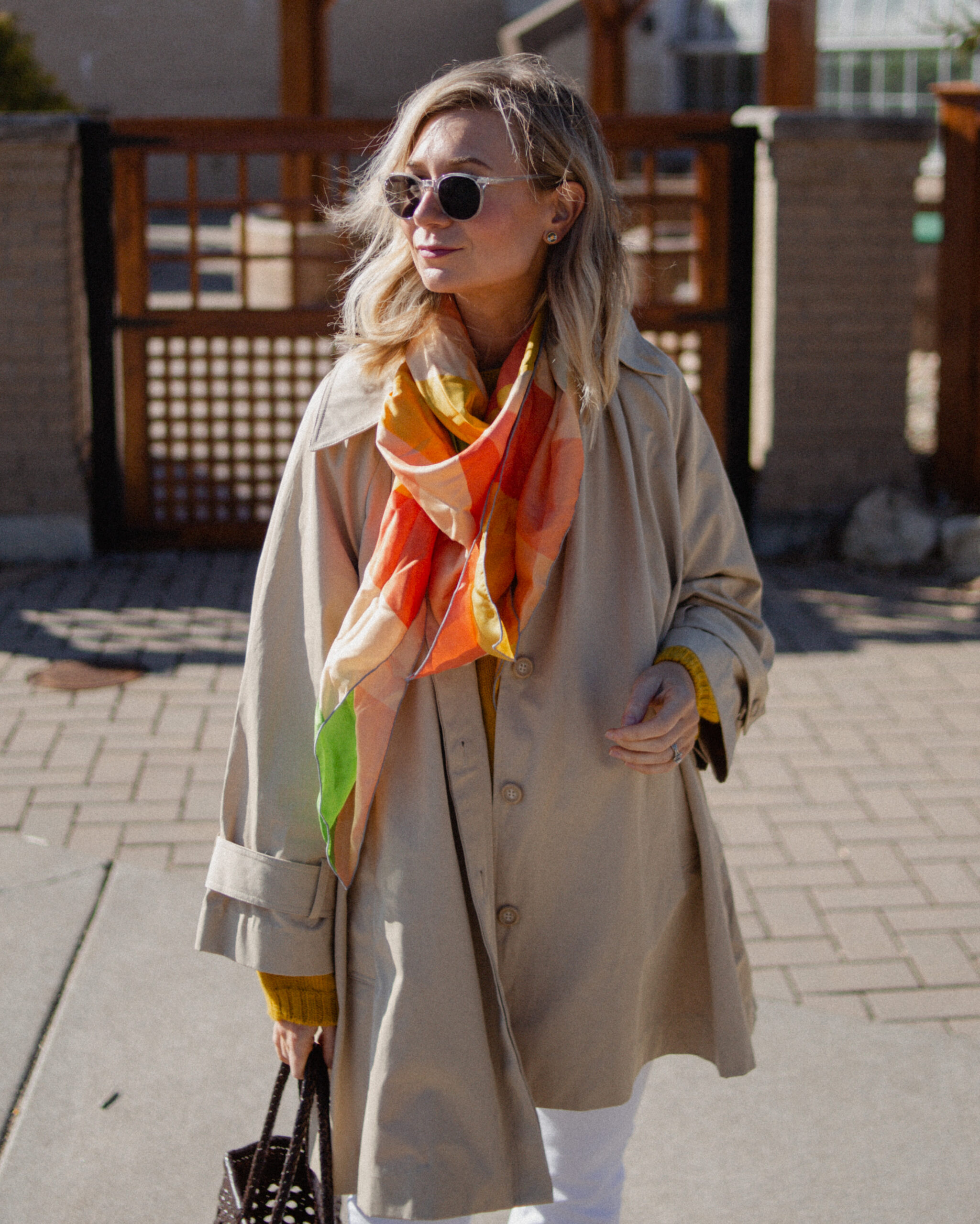 Karin Emily wears a A Classic Trench Coat with a Twist , white jeans, yellow sweater, colorful silk scarf, and green mary jane flats