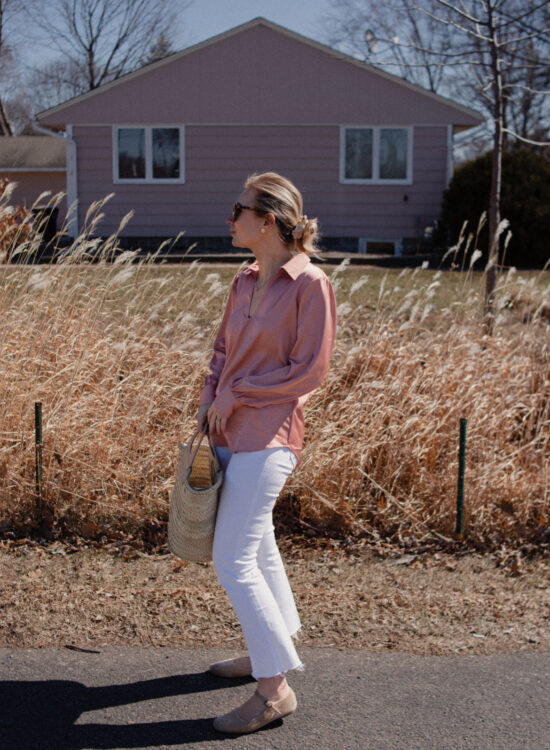 Karin Emily wears a pink satin blouse over white jeans paired with nude mary jane flats and a hereu basket bag