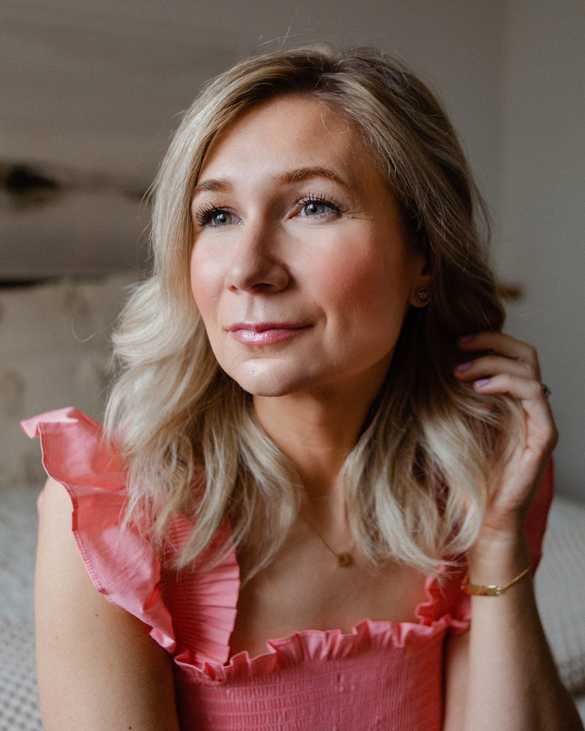 Karin Emily wears a bright pink dress while sitting on a bed sharing her Sephora VIB sale picks