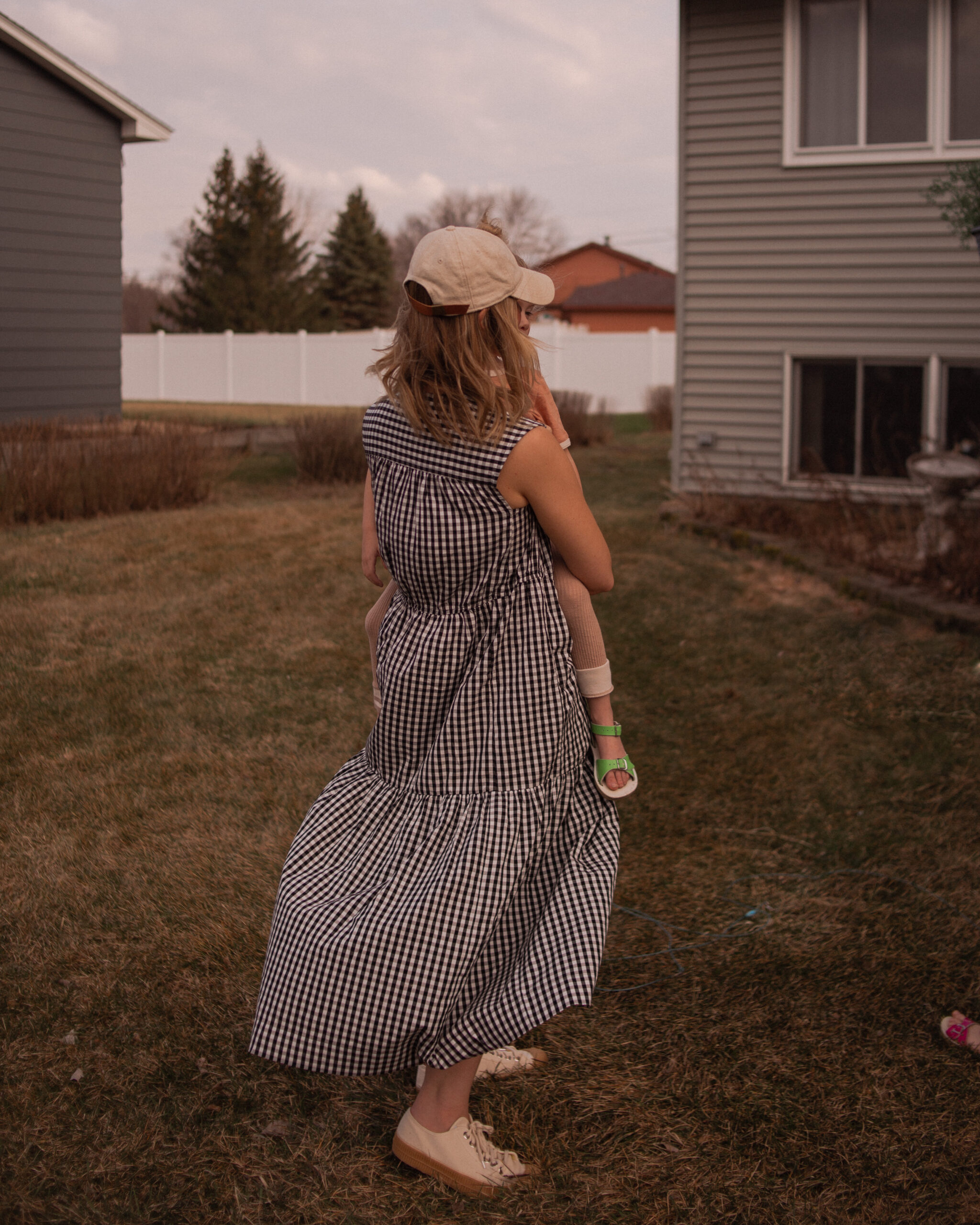 Karin Emily wears a gingham maxi dress from Everlane with canvas sneakers and a neutral baseball hat