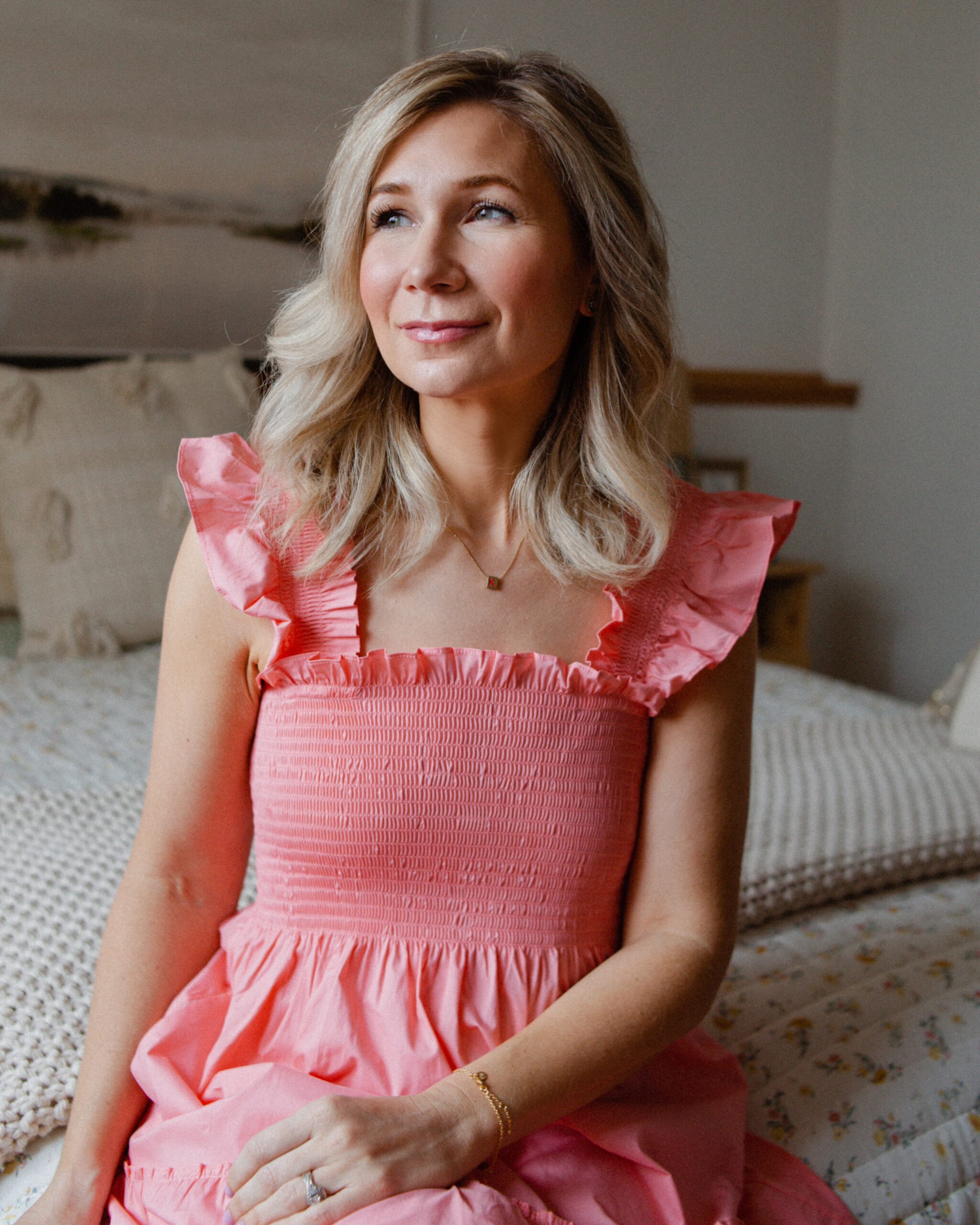 Karin Emily wears a bright pink dress while sitting on a bed sharing her Sephora VIB sale picks