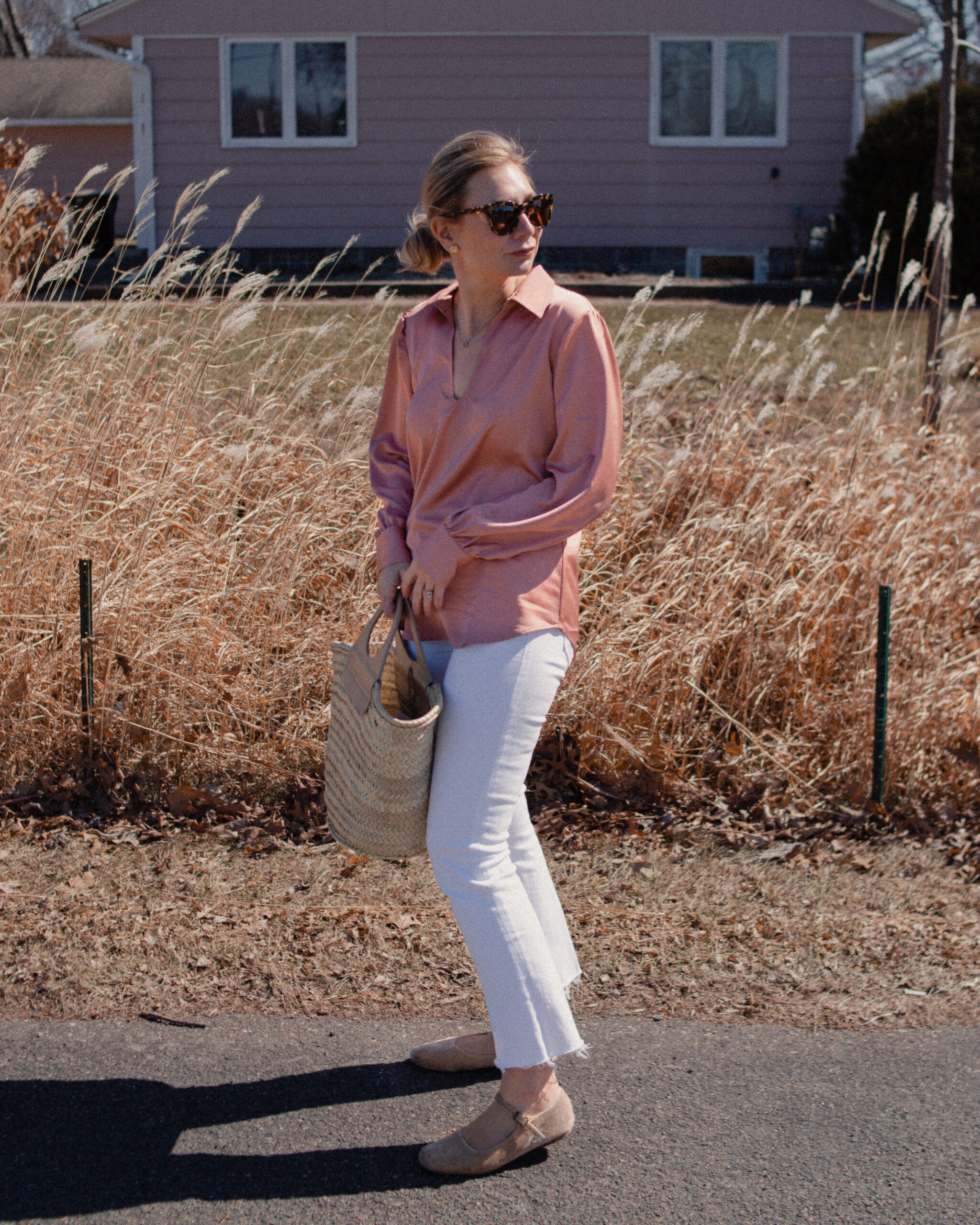 Karin Emily wears a pink satin blouse over white jeans paired with nude mary jane flats and a hereu basket bag