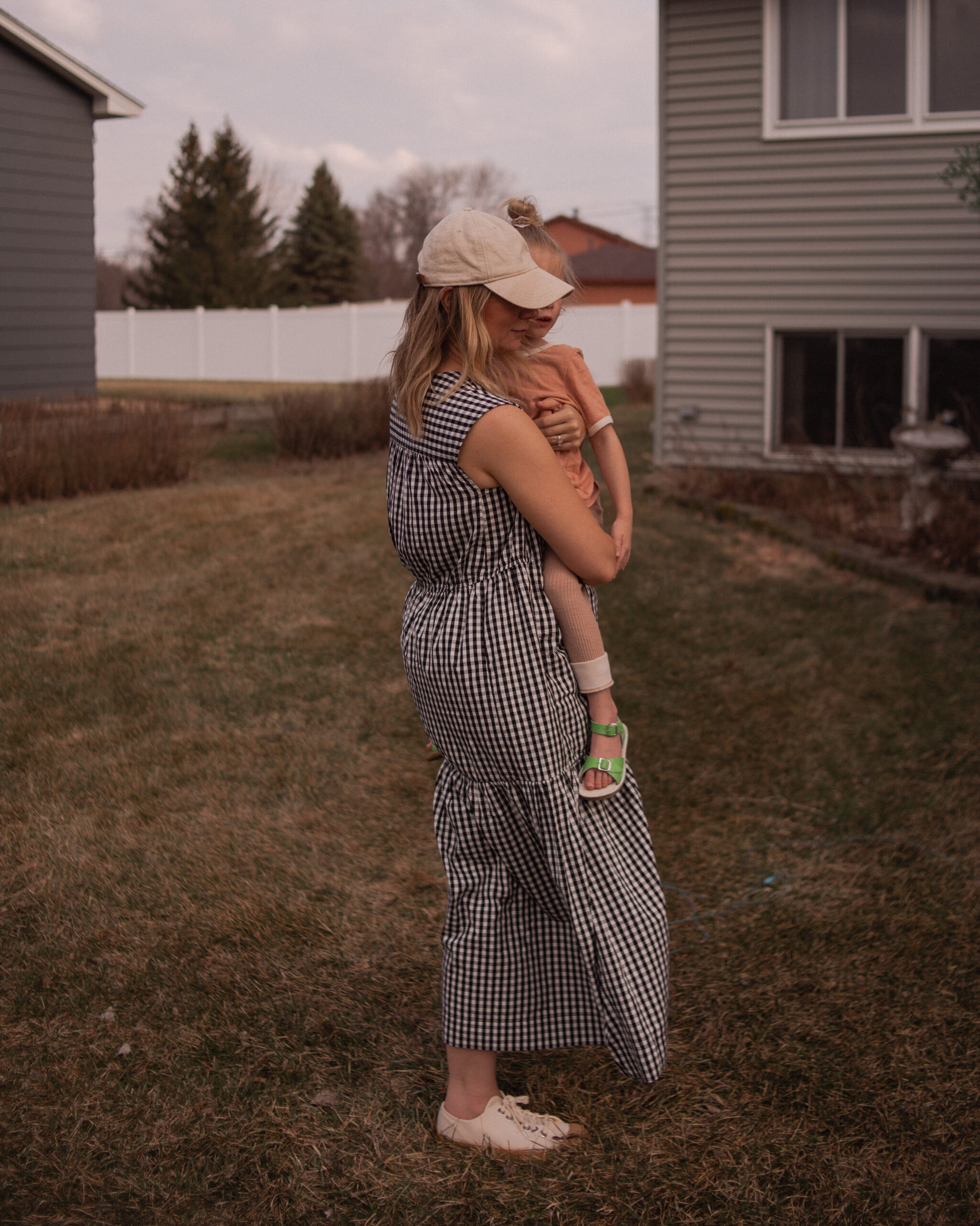 Karin Emily wears a gingham maxi dress from Everlane with canvas sneakers and a neutral baseball hat