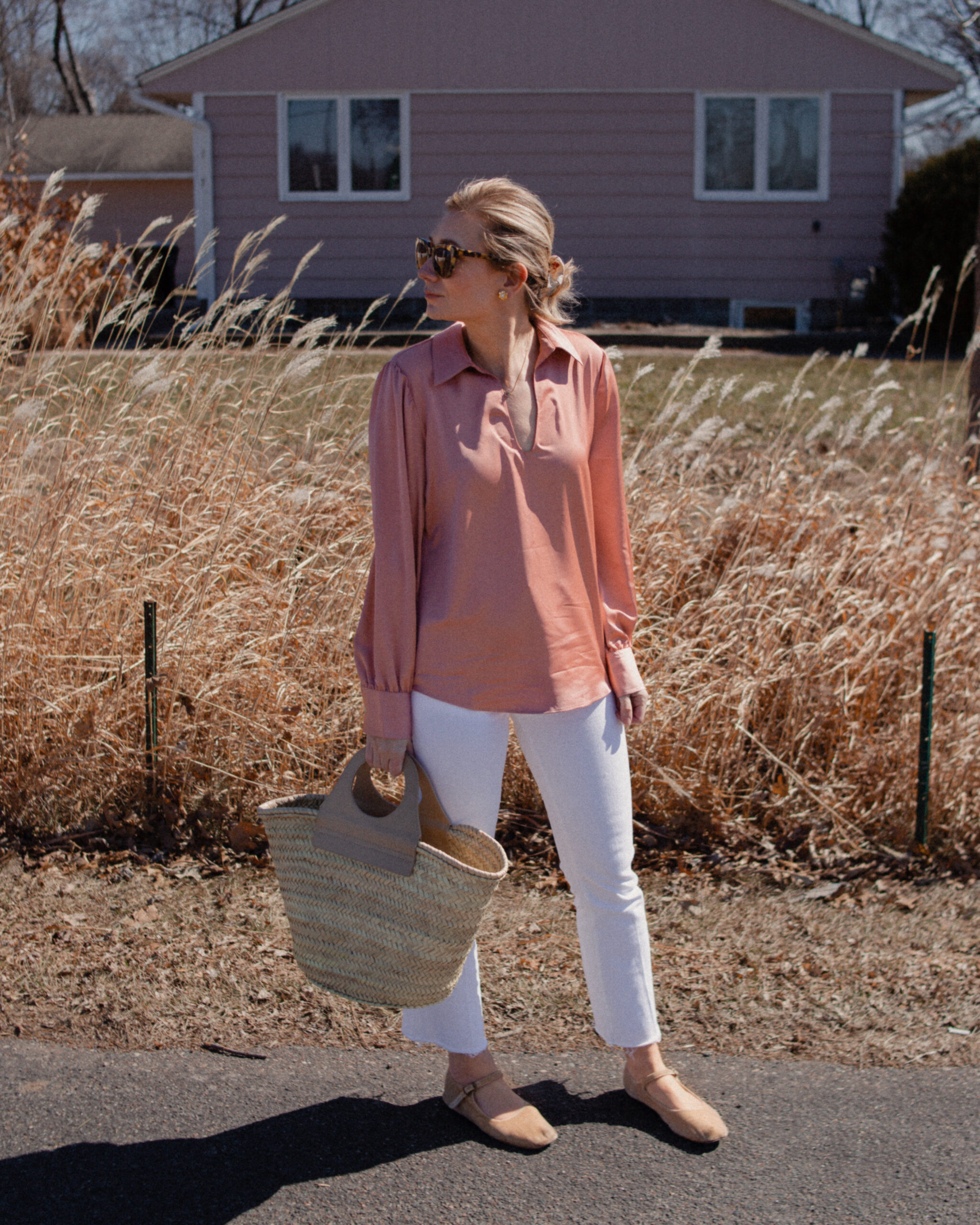 Karin Emily wears a pink satin blouse over white jeans paired with nude mary jane flats and a hereu basket bag