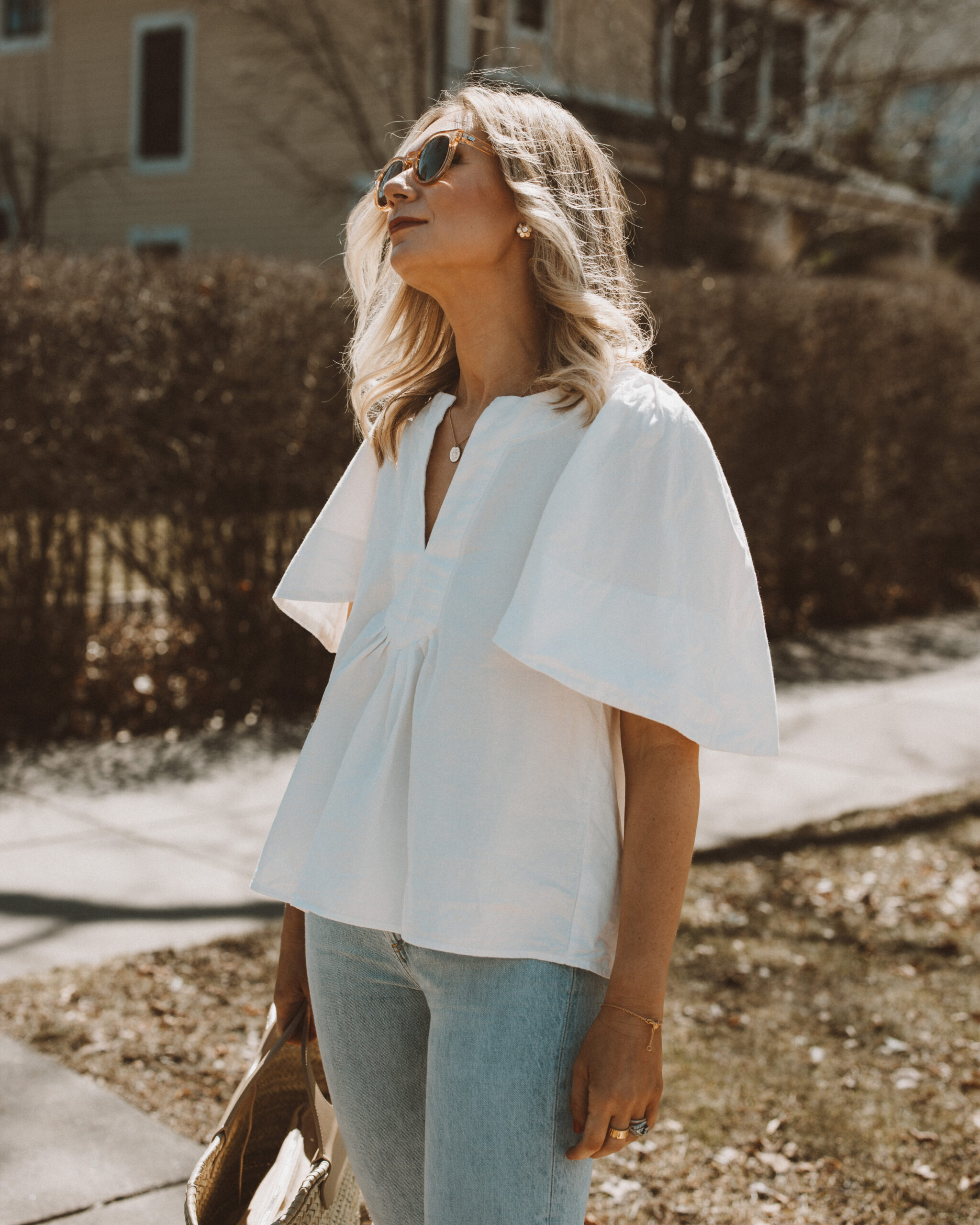 Karin Emily wears a spring top with a pair of light blue wash riley jeans from Agolde and clear framed sunglasses