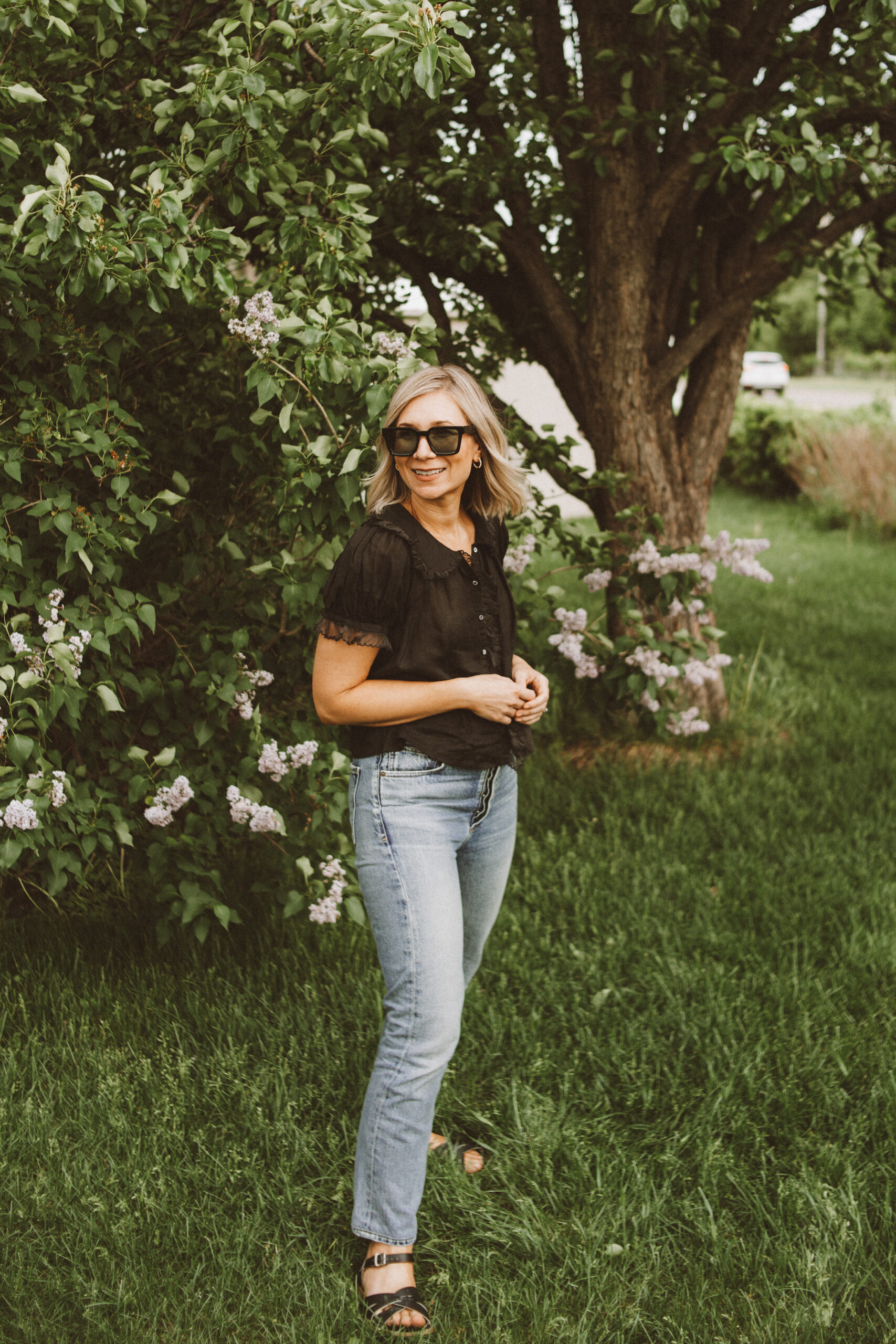 Karin Emily wears one of her favorite romantic blouses for summer with a pair of jeans, black sunglasses, and black sandals