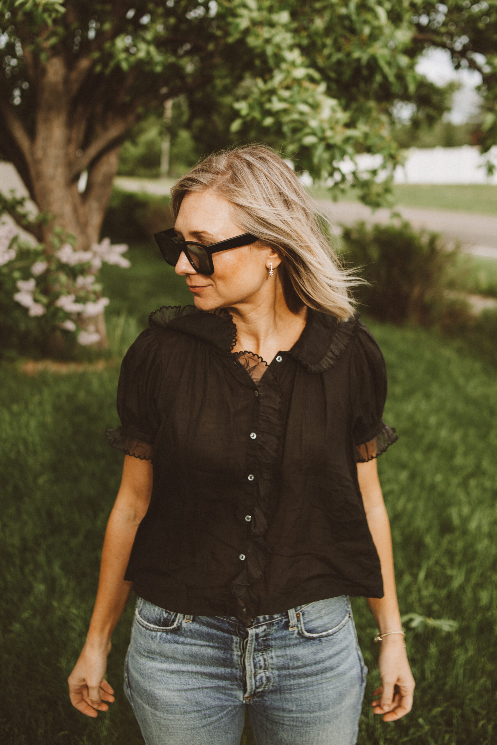 Karin Emily wears one of her favorite romantic blouses for summer with a pair of jeans, black sunglasses, and black sandals