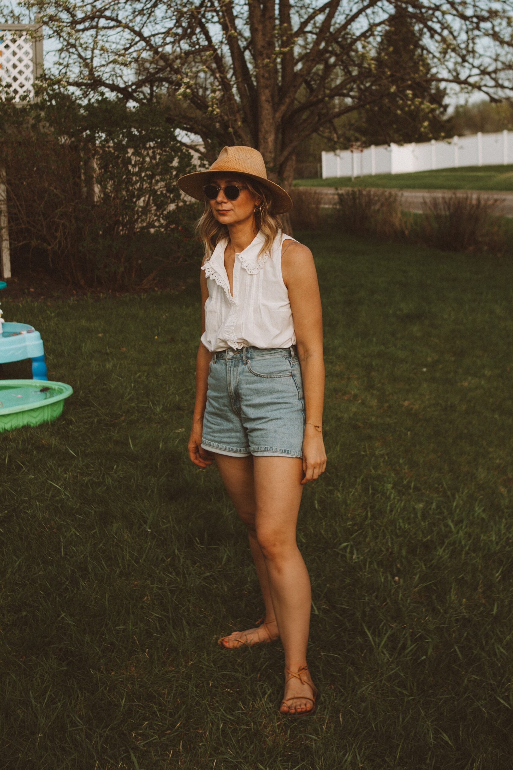 Karin Emily wears white tops from Sezane with a pair of Everlane denim shorts, a janessa leone hat, and minimal sandals