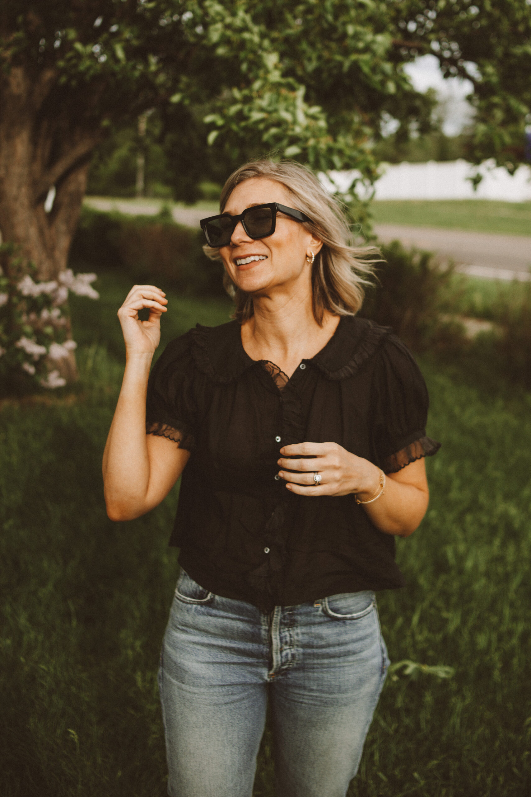 Karin Emily wears one of her favorite romantic blouses for summer with a pair of jeans, black sunglasses, and black sandals