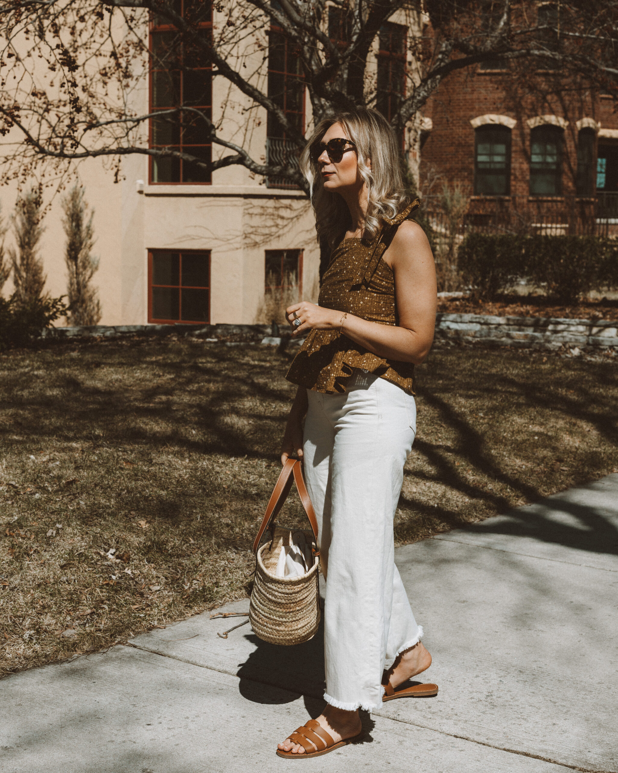 Karin Emily wears a peplum top from Madewell, a pair of wide leg jeans from AYR, a Poolside Basket Bag and a pair of Fisherman sandal slides from Madewell