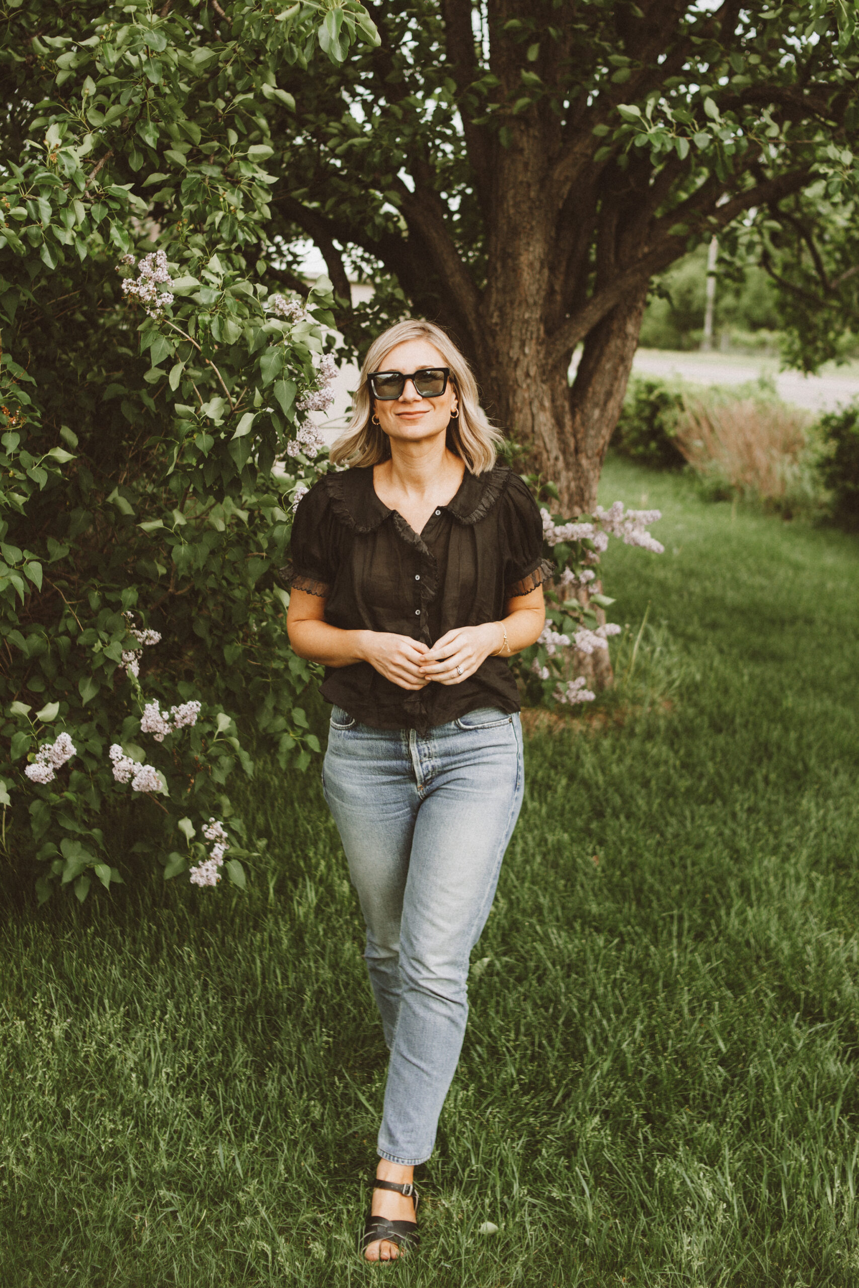 Karin Emily wears one of her favorite romantic blouses for summer with a pair of jeans, black sunglasses, and black sandals