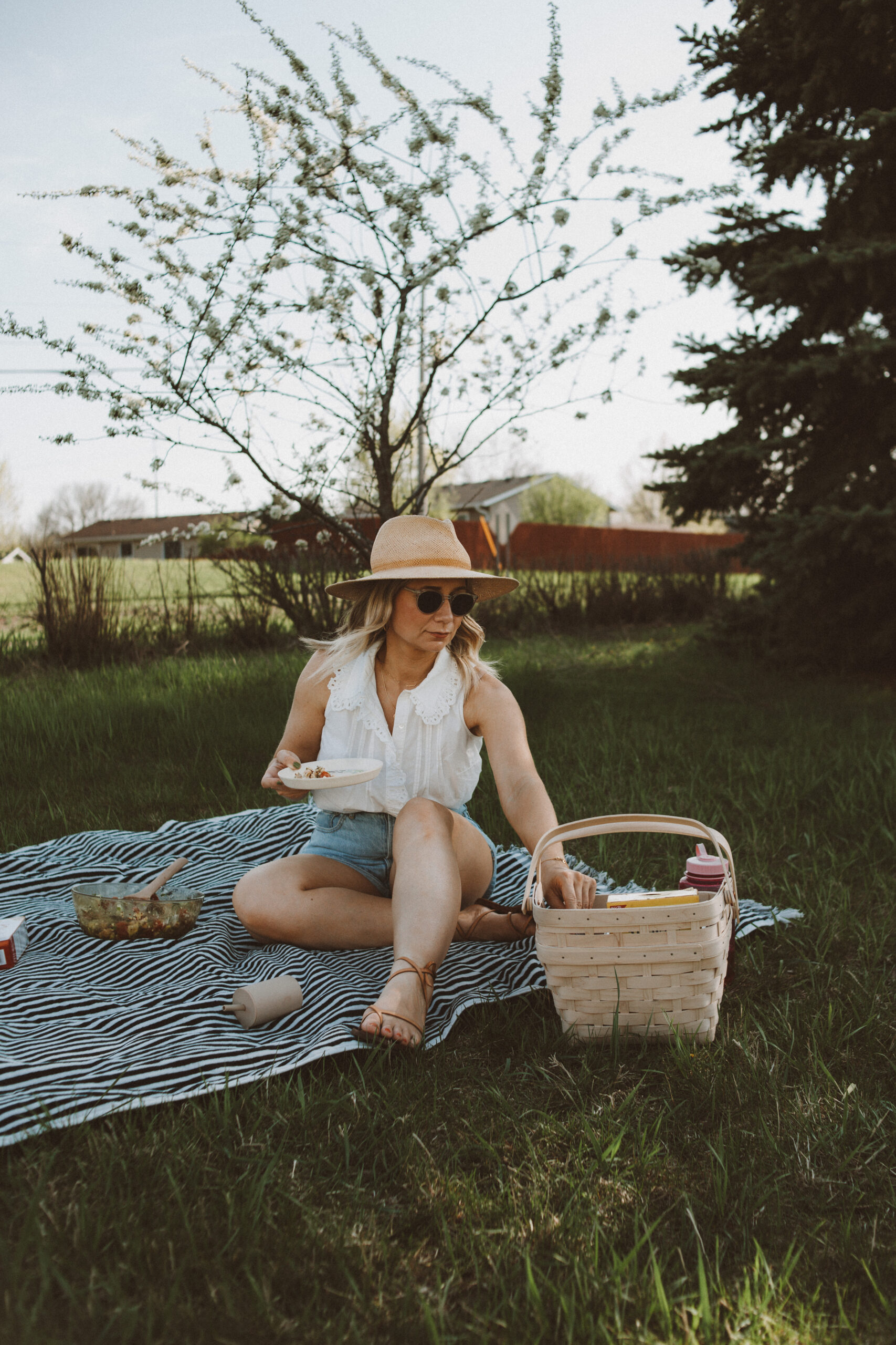 Karin Emily wears white tops from Sezane with a pair of Everlane denim shorts, a janessa leone hat, and minimal sandals