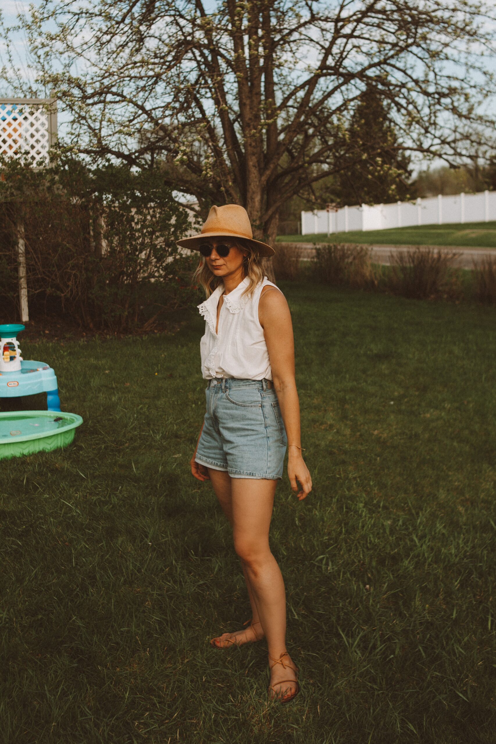 Karin Emily wears white tops from Sezane with a pair of Everlane denim shorts, a janessa leone hat, and minimal sandals