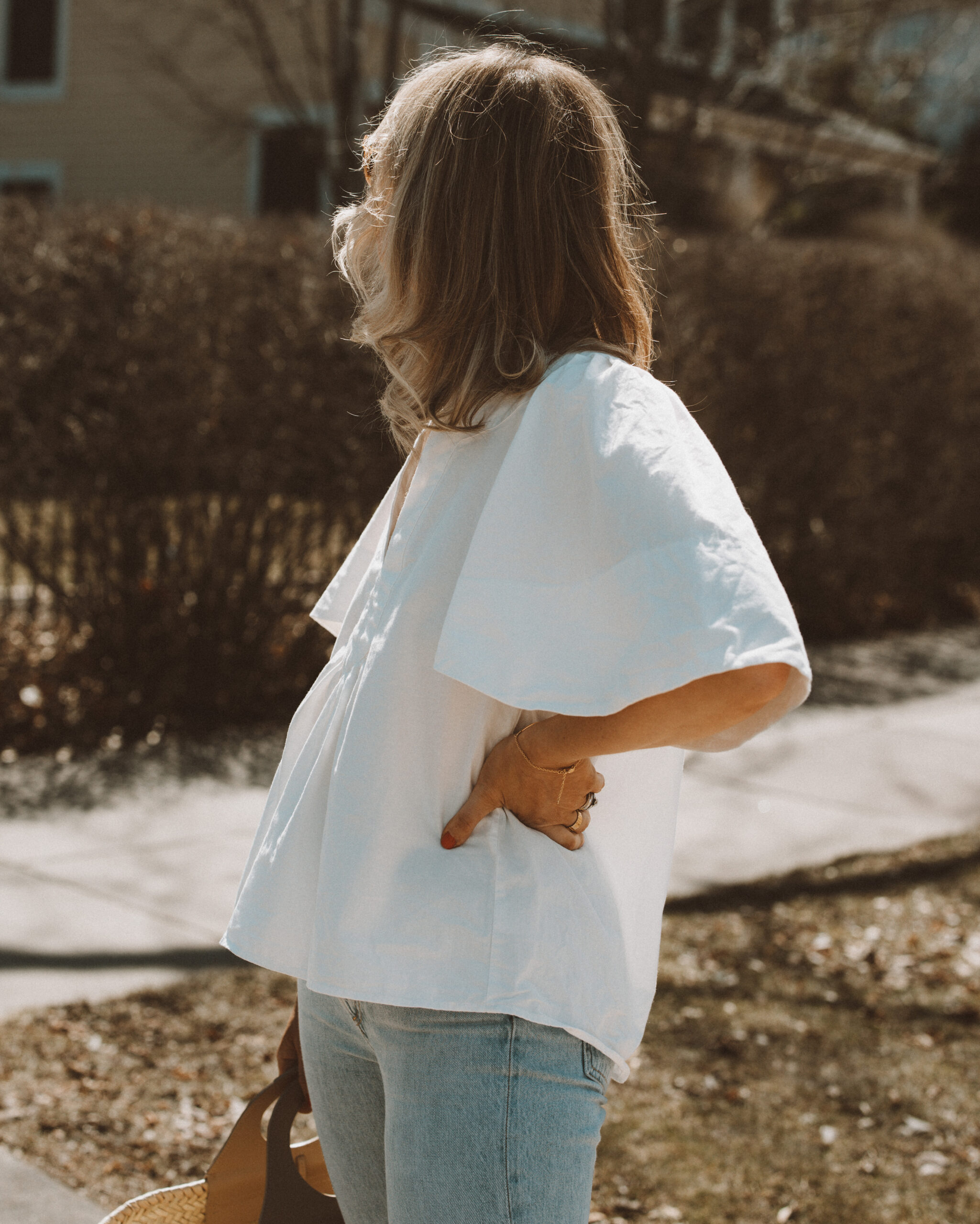 Karin Emily wears a white flutter sleeve blouse with a pair of light blue wash riley jeans from Agolde