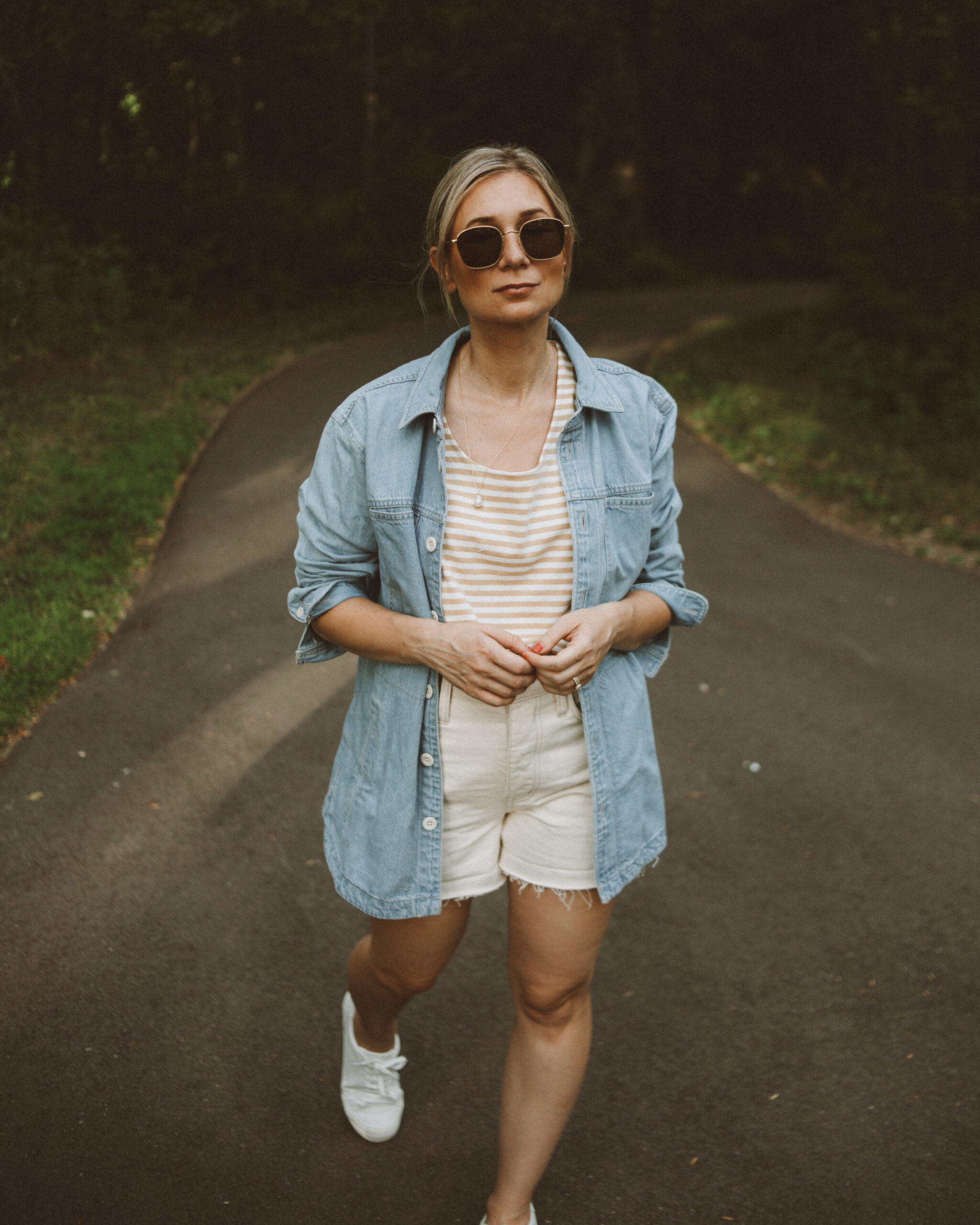 Karin Emily wears a striped tee, cream jean shorts, white sneakers and a light wash denim shirt jacket