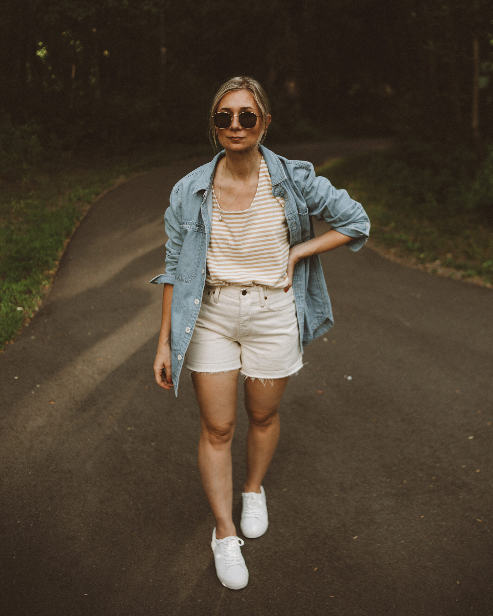 Karin Emily wears a striped tee, cream jean shorts, white sneakers and a light wash denim shirt jacket