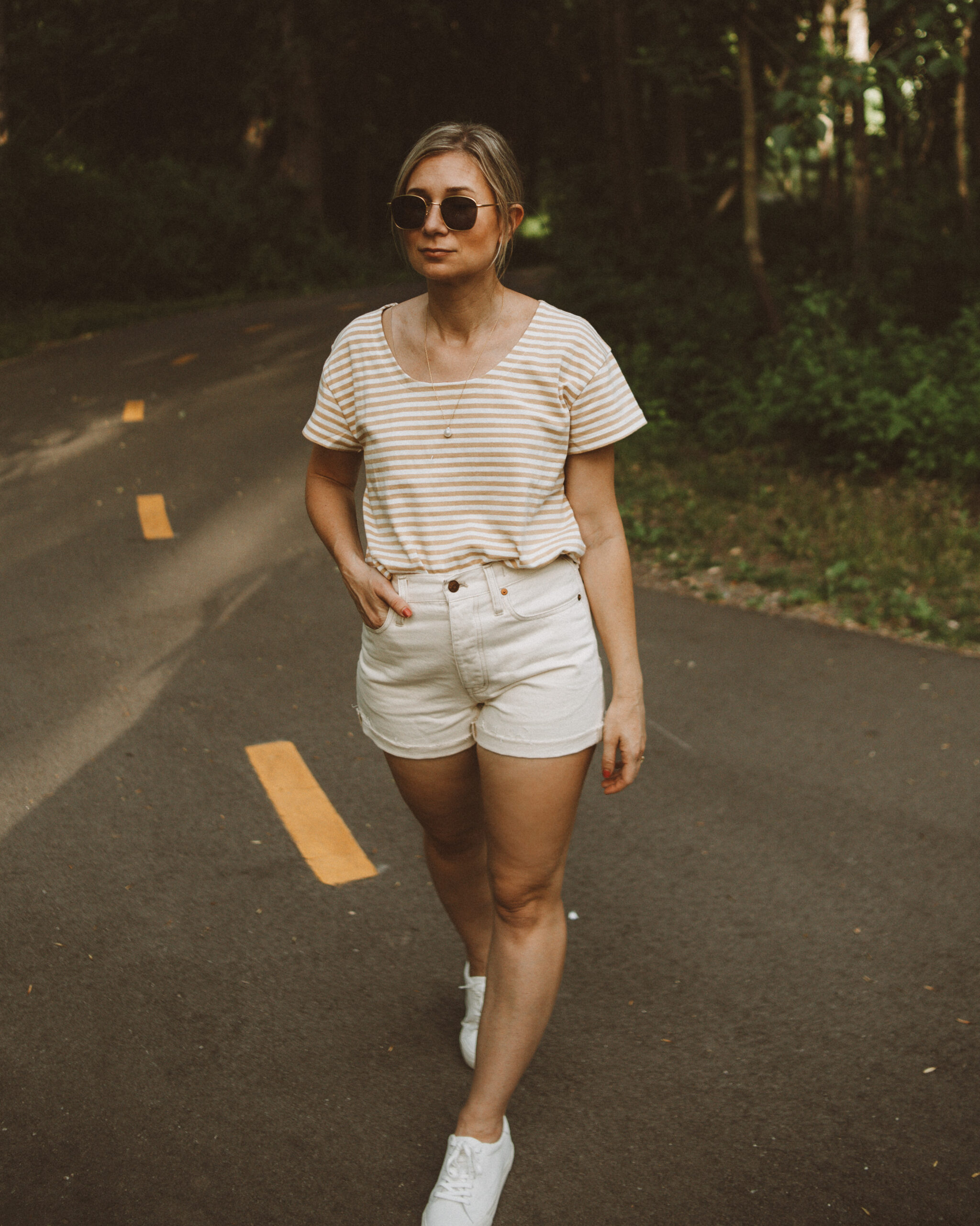 Karin Emily wears a striped tee, white sneakers, and cream jean shorts