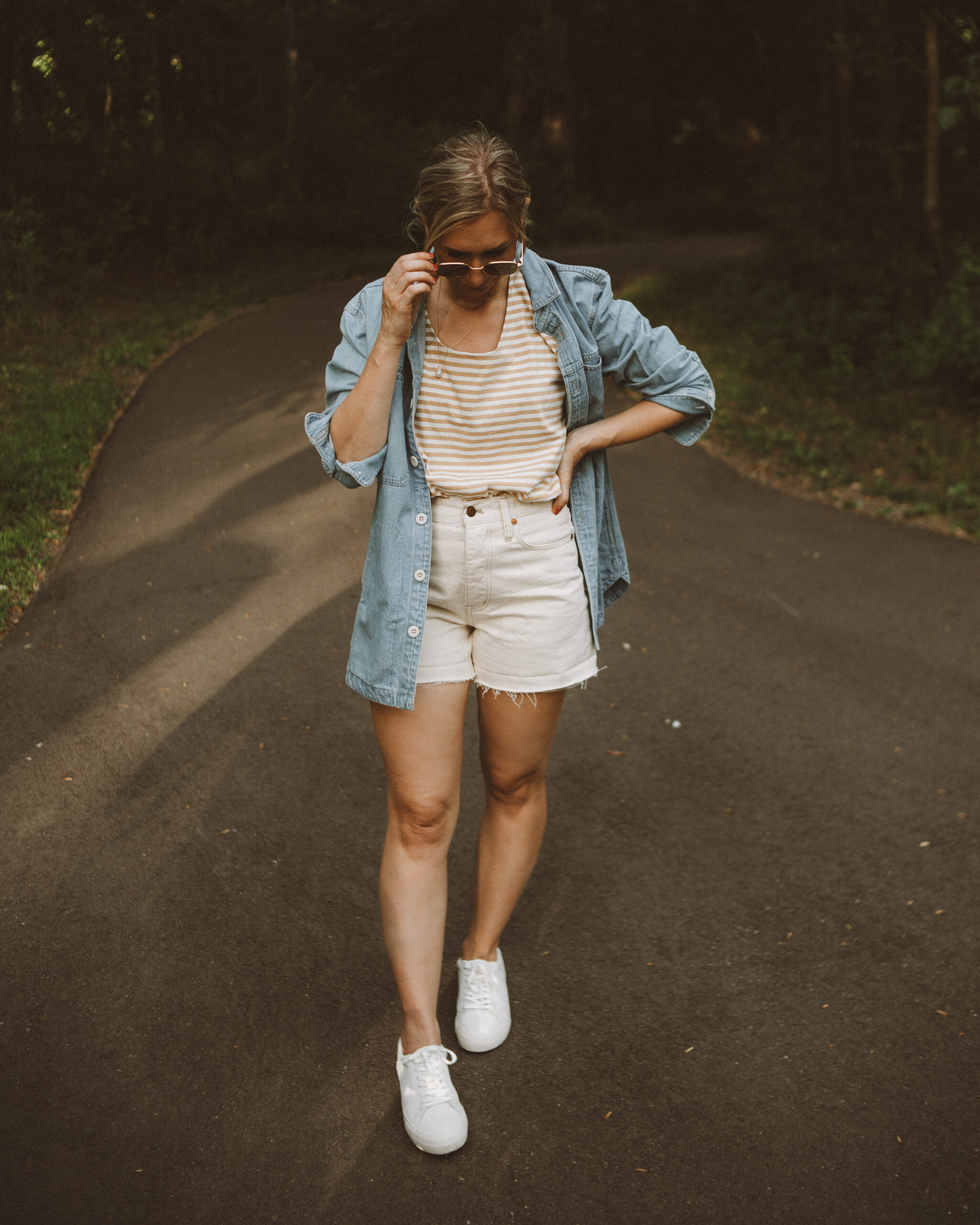 Karin Emily wears a striped tee, cream jean shorts, white sneakers and a light wash denim shirt jacket