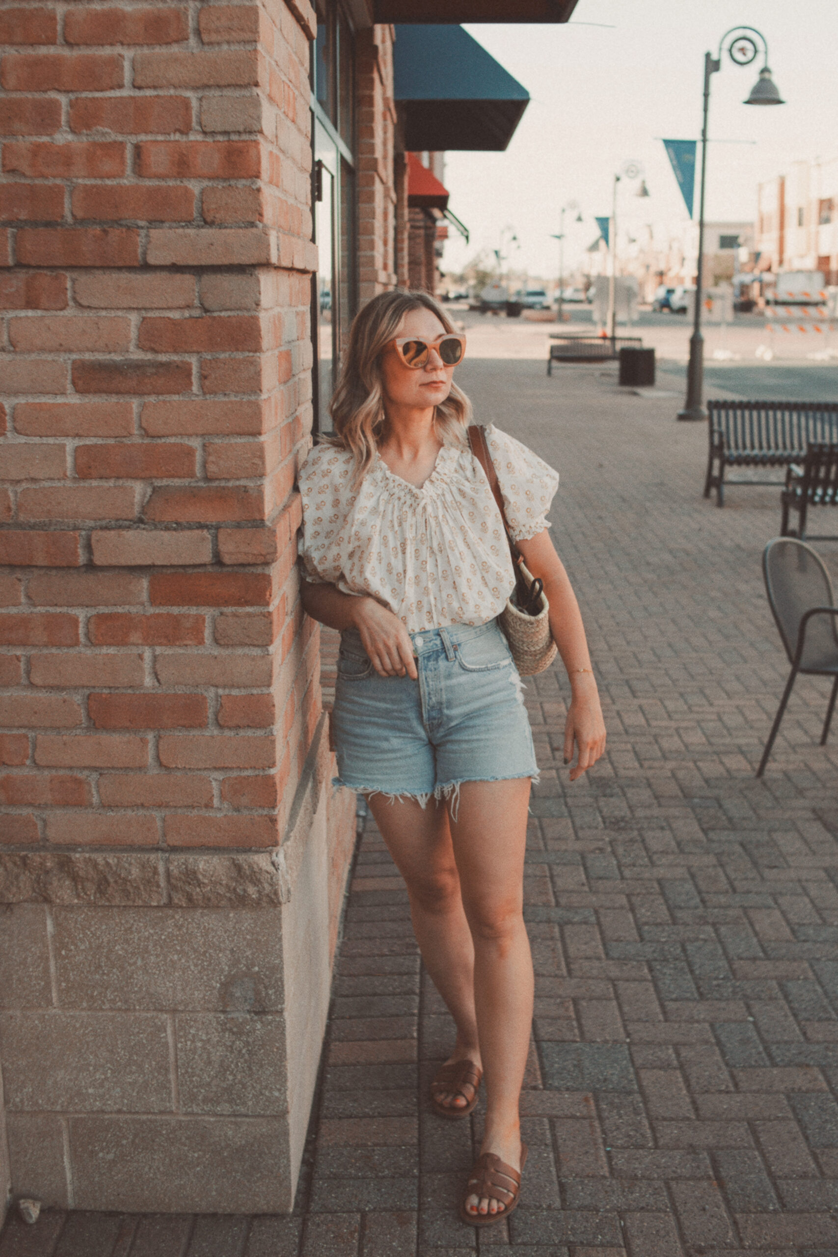 Karin Emily wears a floral doen top, light wash jean shorts, and brown strappy sandals