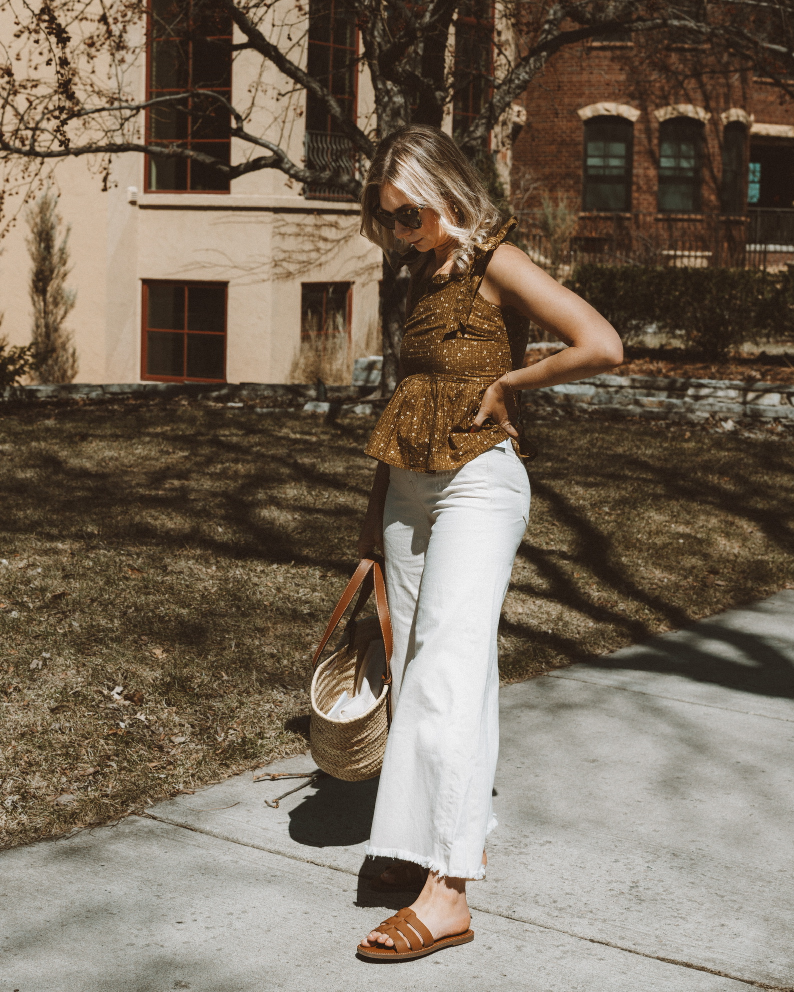 Karin Emily wears a brown peplum tank, white wide leg jeans, and brown designer dupe sandals