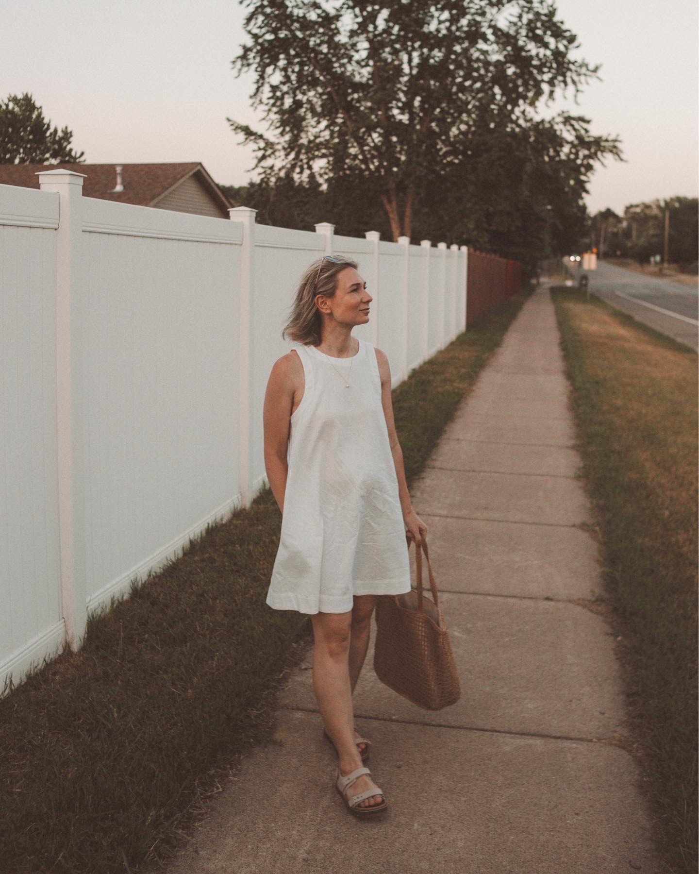 Karin Emily wears a white linen mini dress with a light pair of chunky dad sandals and a woven basket bag