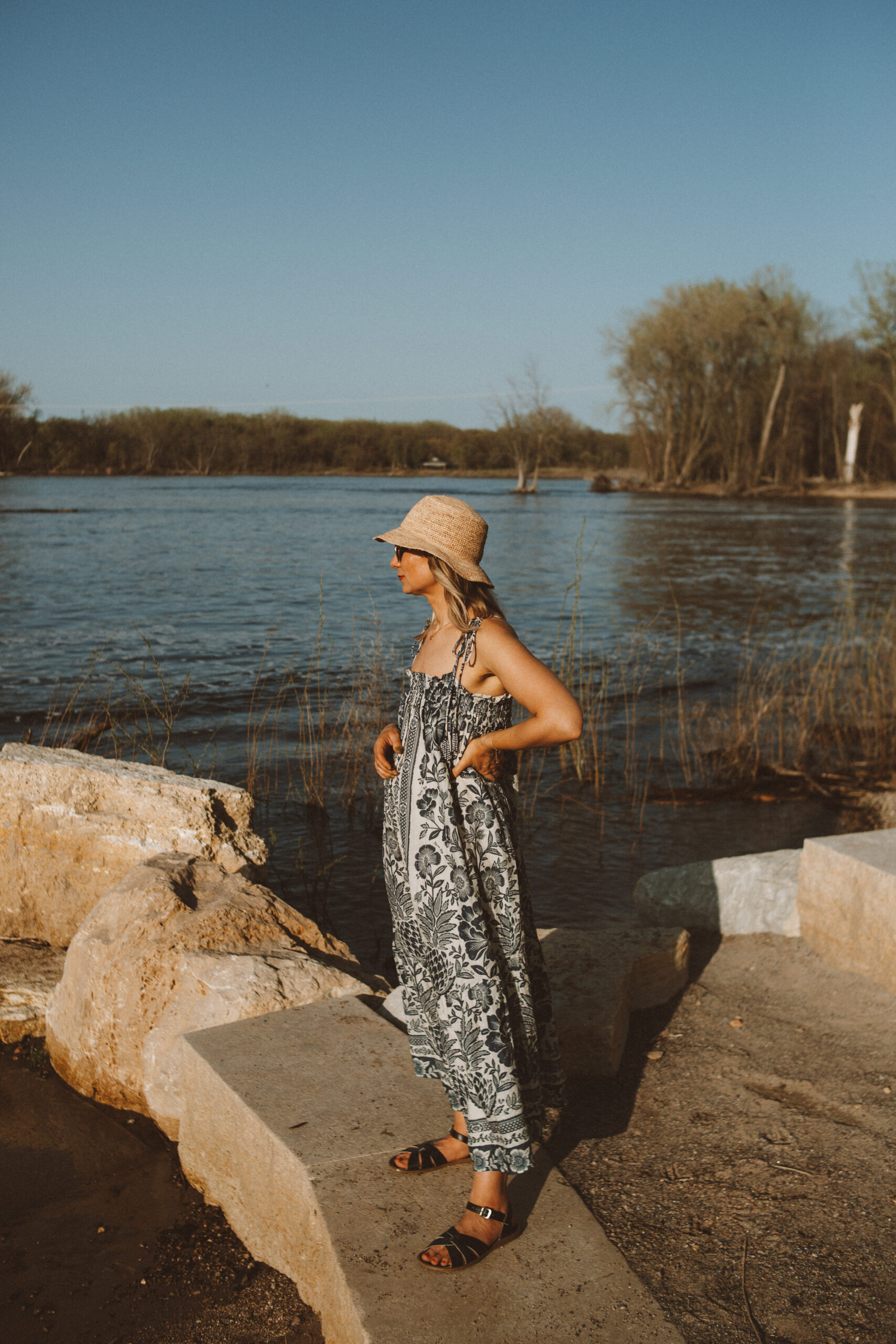 Karin Emily wears a white and blue farm rio dress, woven bucket hat, and black saltwater sandals