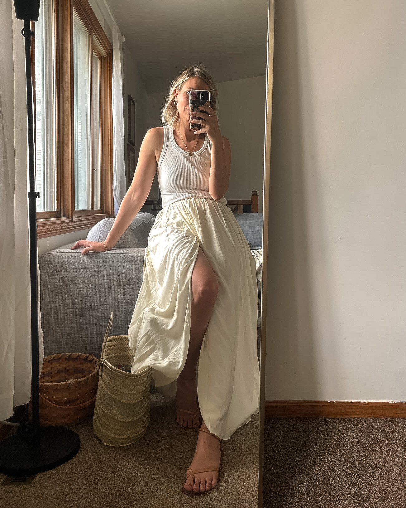 Karin Emily wears a cream wrap skirt and white tank top with white sunglasses and strappy sandals