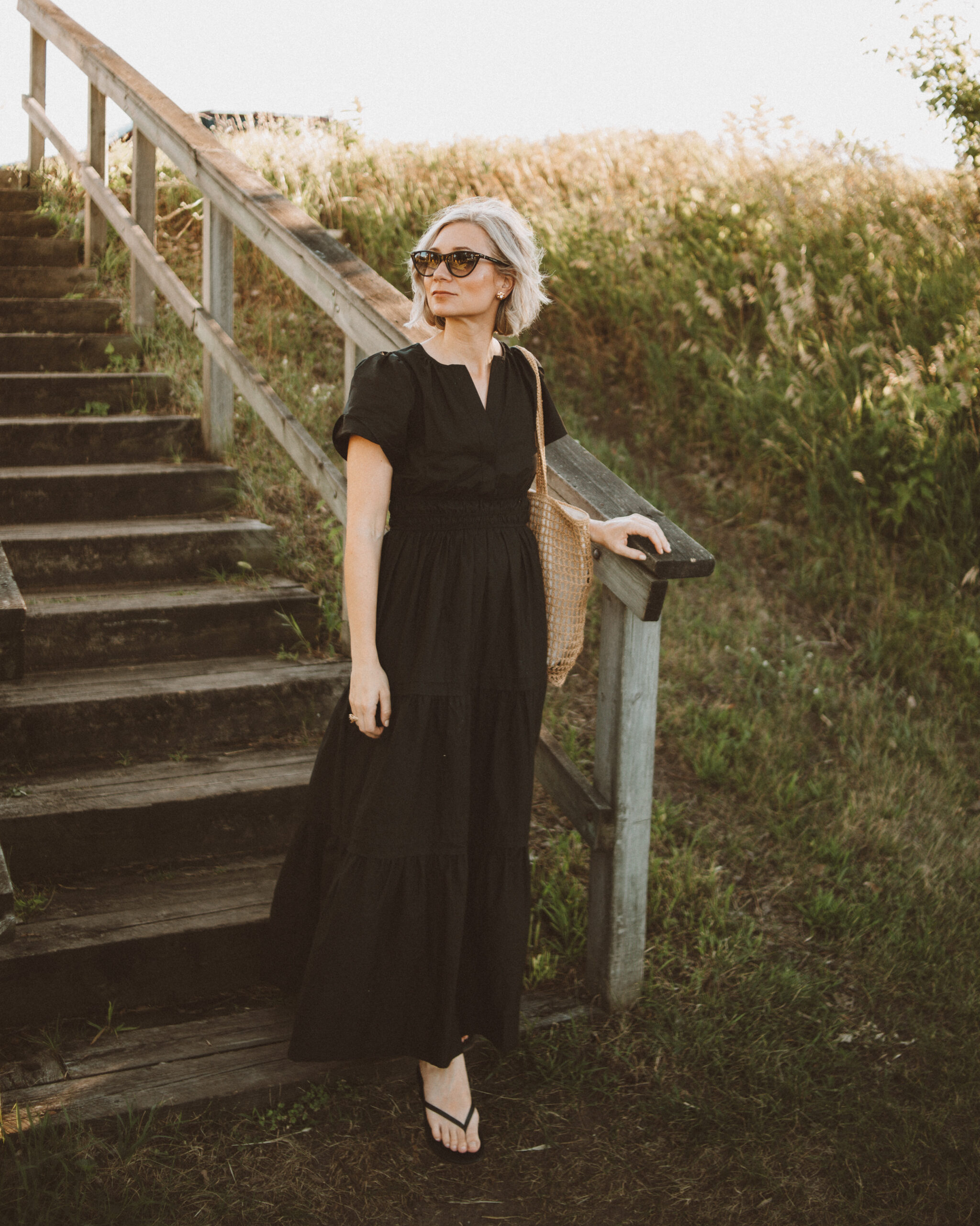Karin Emily wears a black maxi dress with black sandals and a woven bag