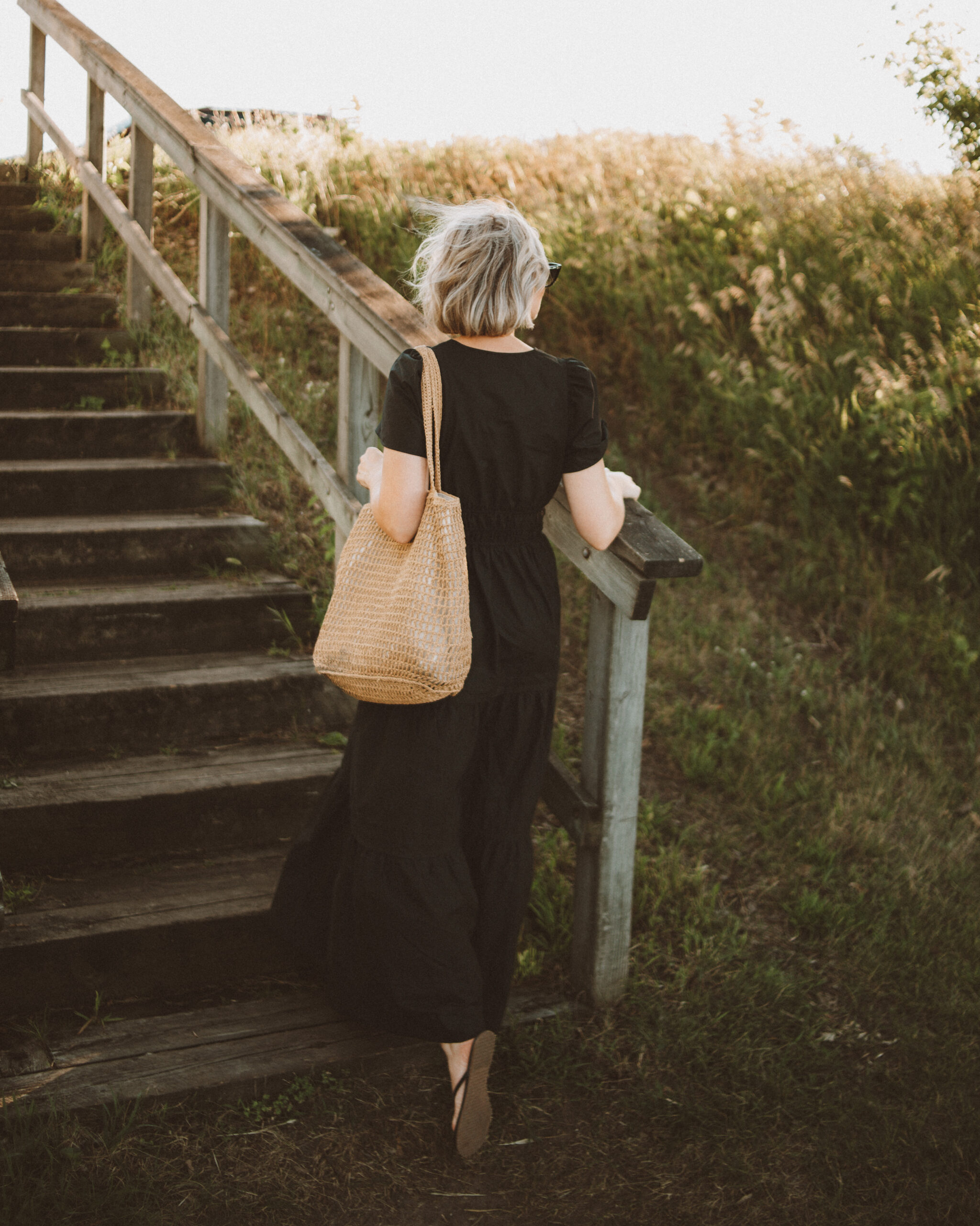 Karin Emily wears a black maxi dress with black sandals and a woven bag