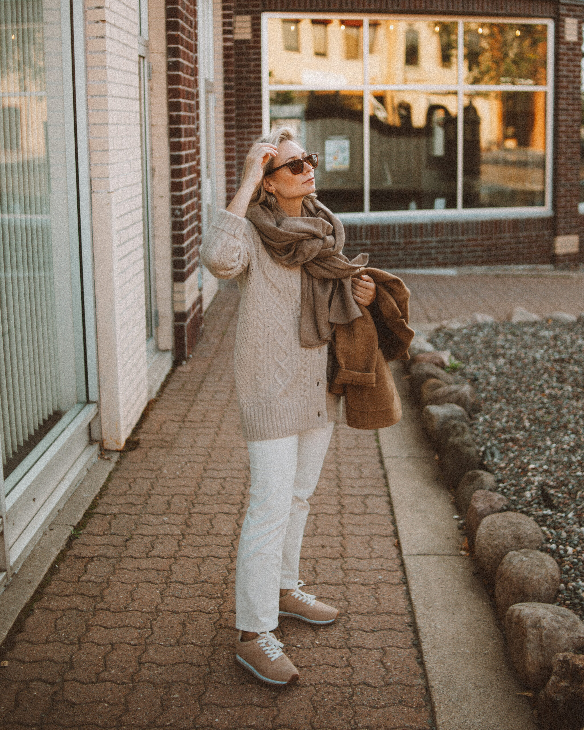 Karin Emily wears the perfect pair of corduroy pants with a cable knit cardigan, tan sneakers, cashmere scarf, and camel wool blazer coat